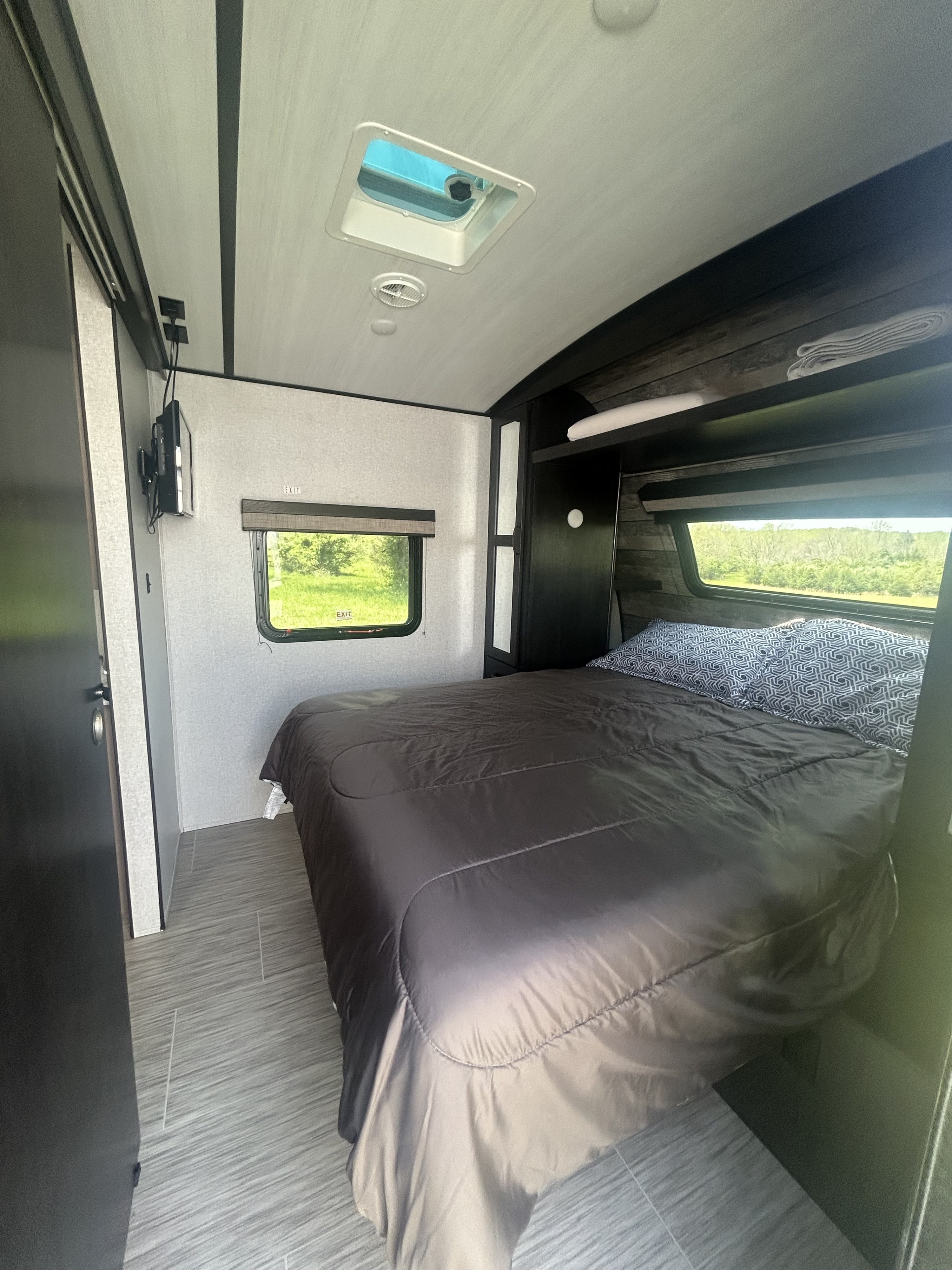 RV rental bedroom: spacious interior with a large bed, patterned pillows, wall-mounted TV, storage, and outdoor window view.. Forest River Surveyor Legend 2021