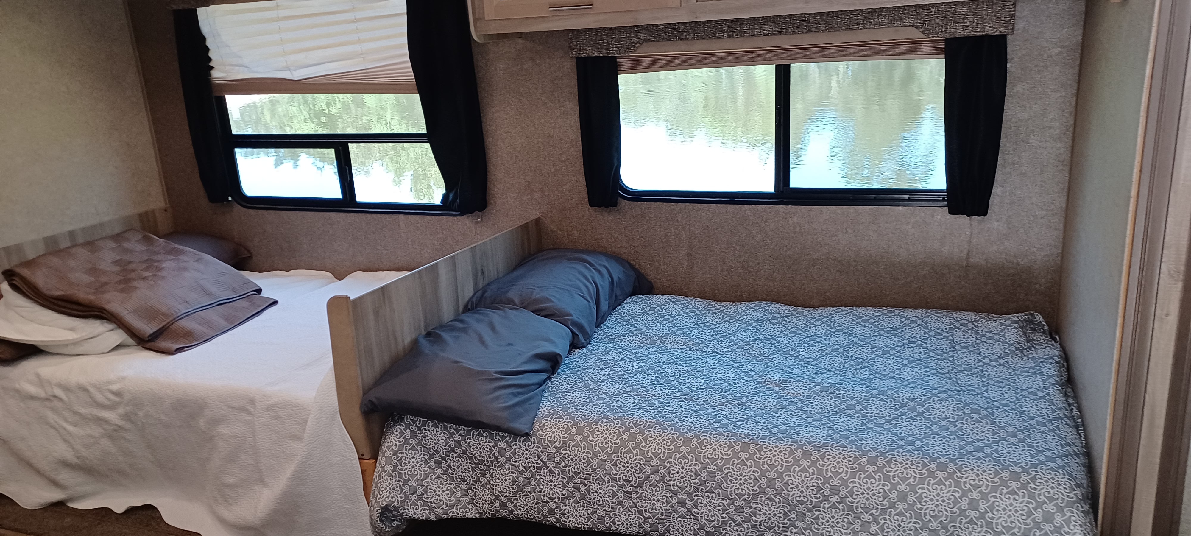 Cozy RV rental interior showing two neatly made beds with light and dark bedding, and scenic water views from large windows.. Forest River Coachmen Catalina SBX 2019