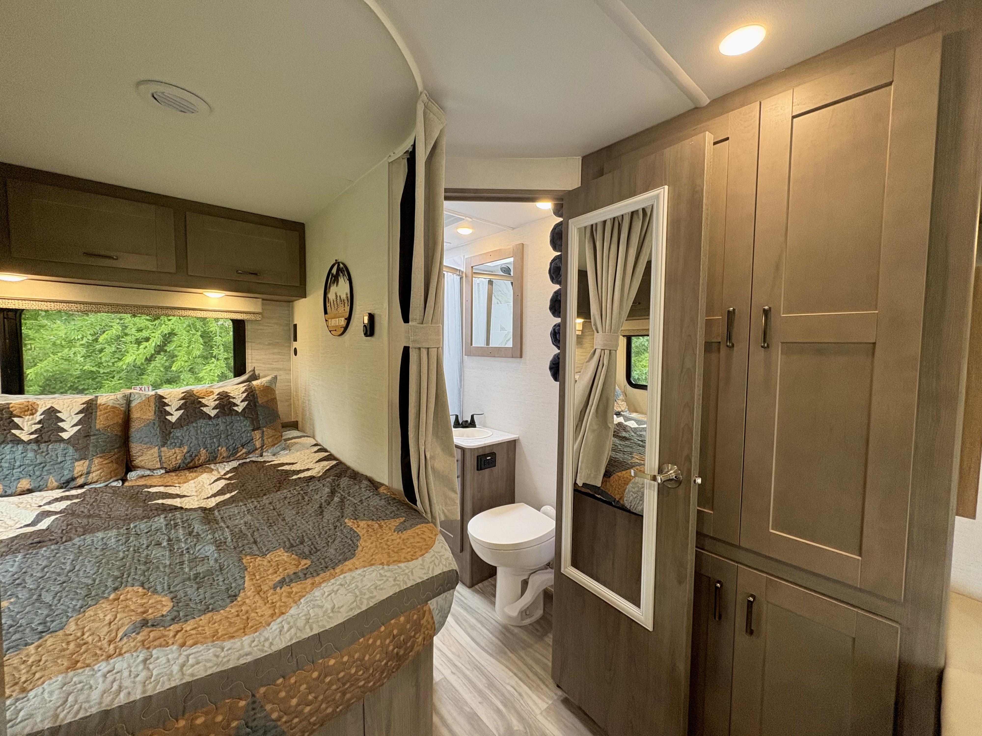 Cozy RV rental bedroom with patterned bedding and window view of trees.. Gulf Stream Conquest 2025