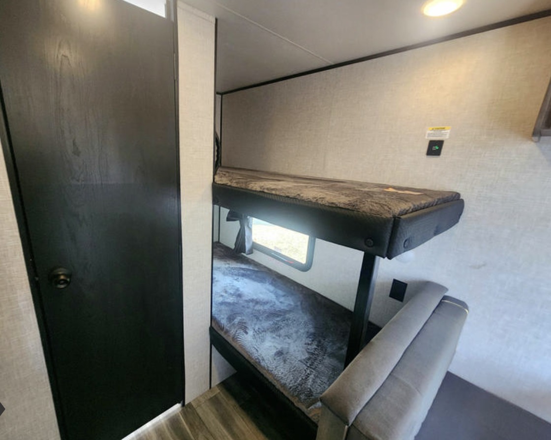 RV rental interior features space-saving stacked bunk beds, a window, and a dark access door.. Jayco Jay Flight SLX 2025