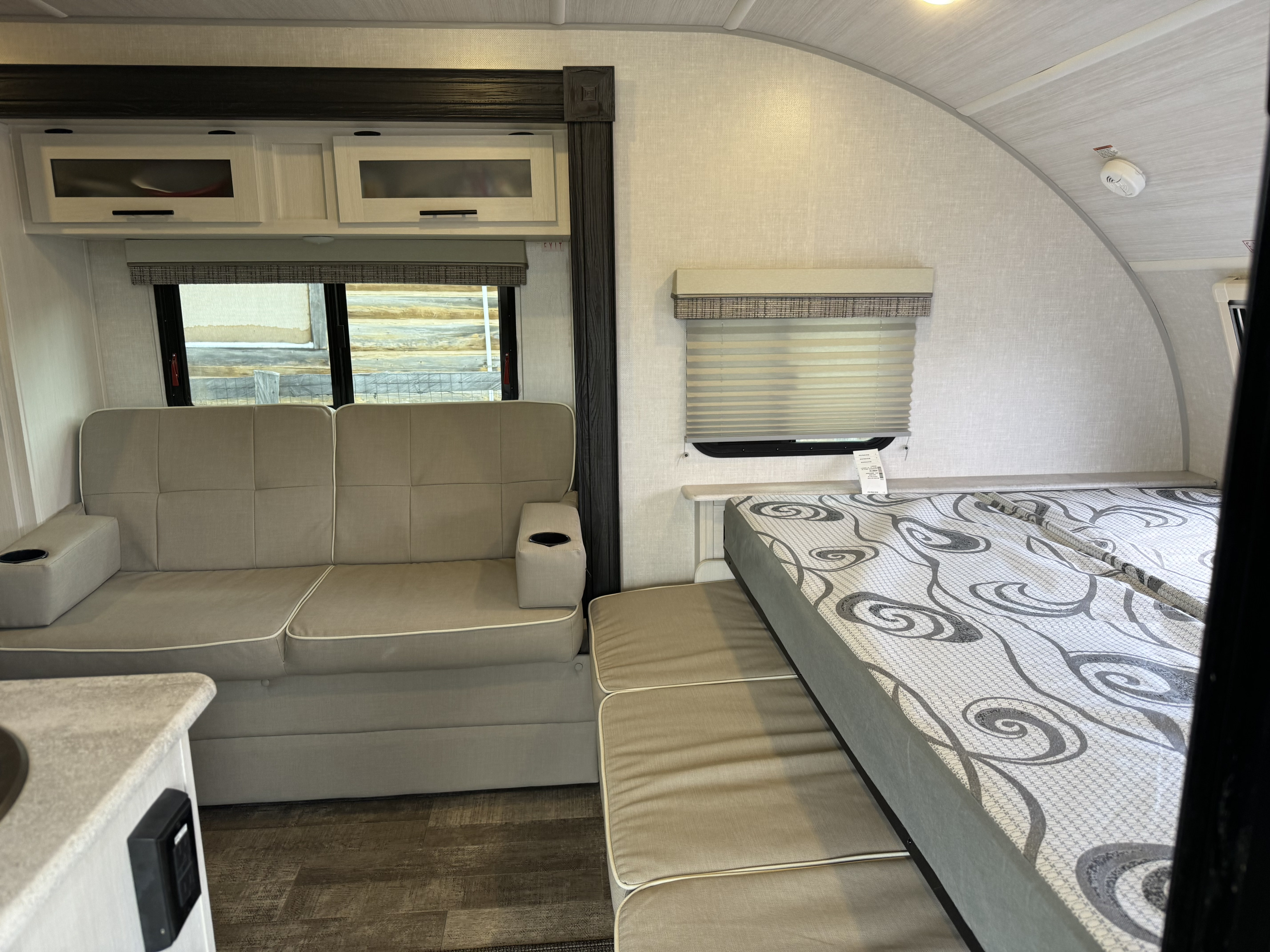 Modern rv rental interior: light-toned sofa with cup holders, patterned bed, overhead cabinets, and wood-look flooring.. R-Pod R-Pod Trailer 2022