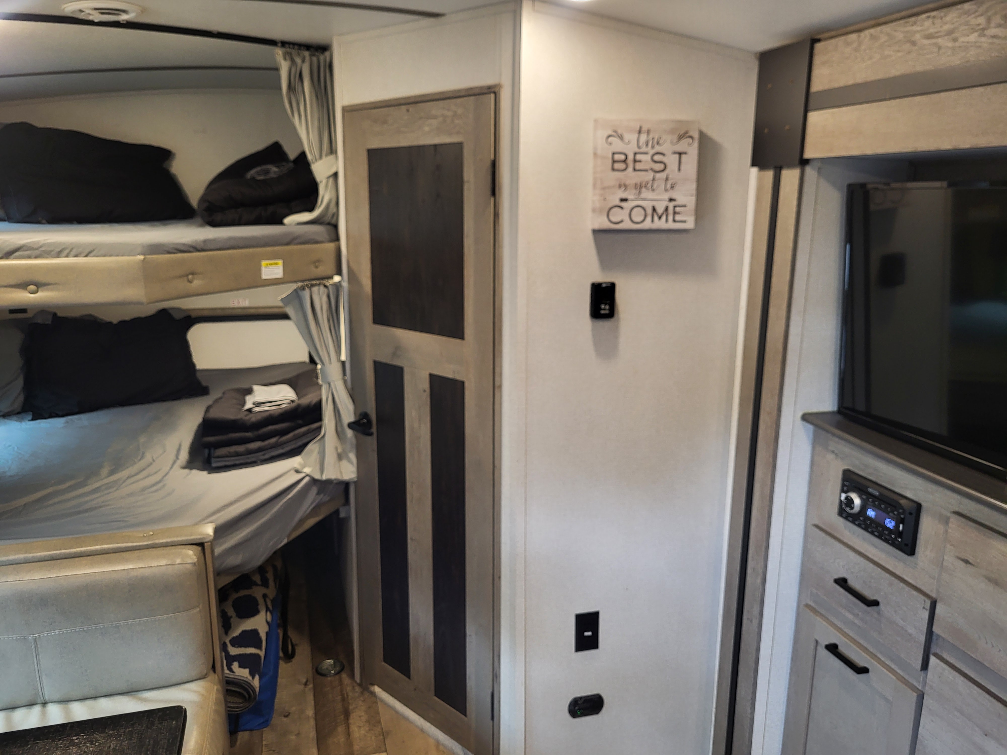 RV rental interior: bunk beds, wooden door, inspirational sign, and media console for cozy journeys.. Keystone Outback 2021