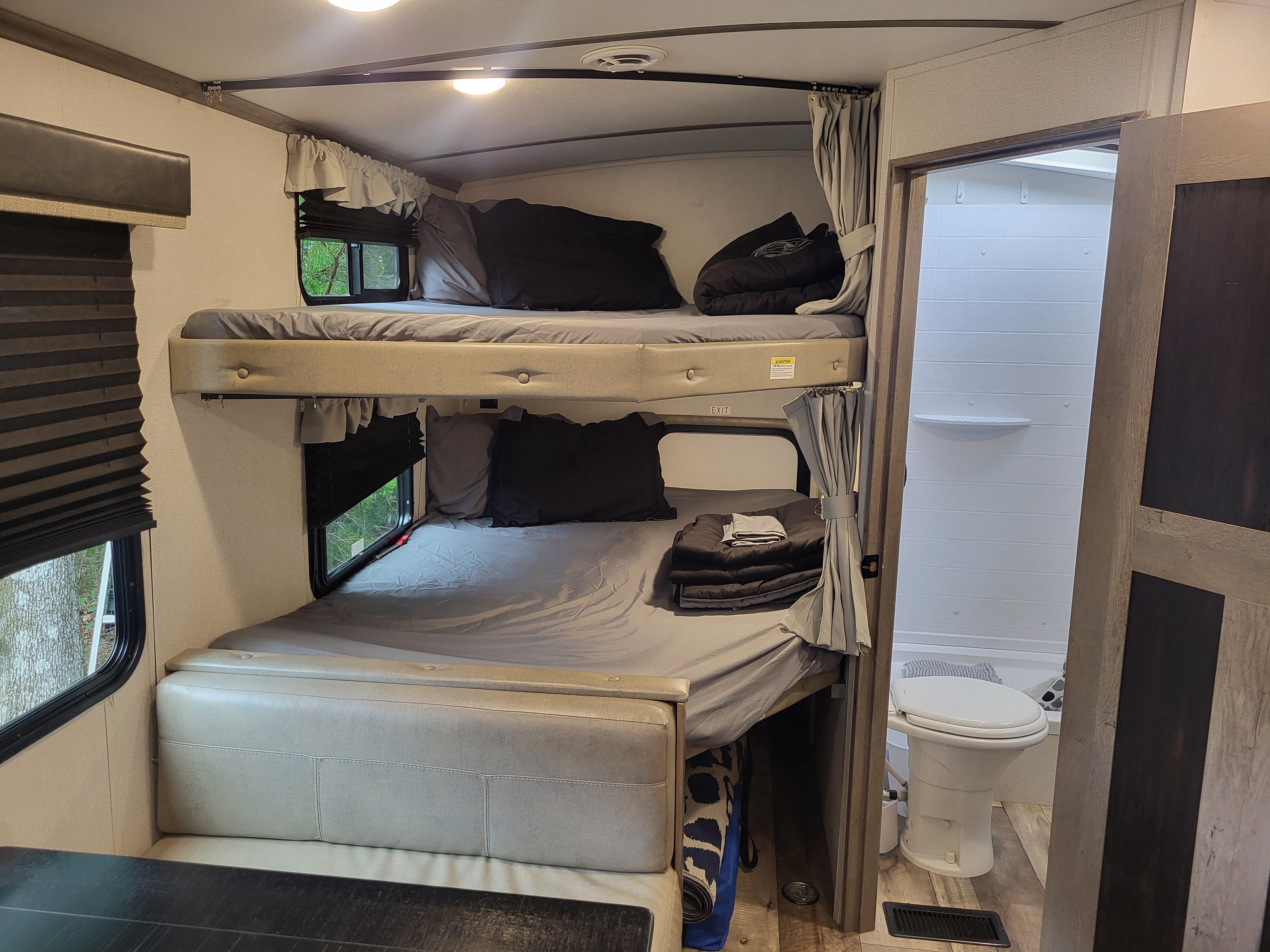 Cozy rv rental interior featuring stacked bunk beds, convertible lower seating, and an adjacent compact bathroom.. Keystone Outback 2021