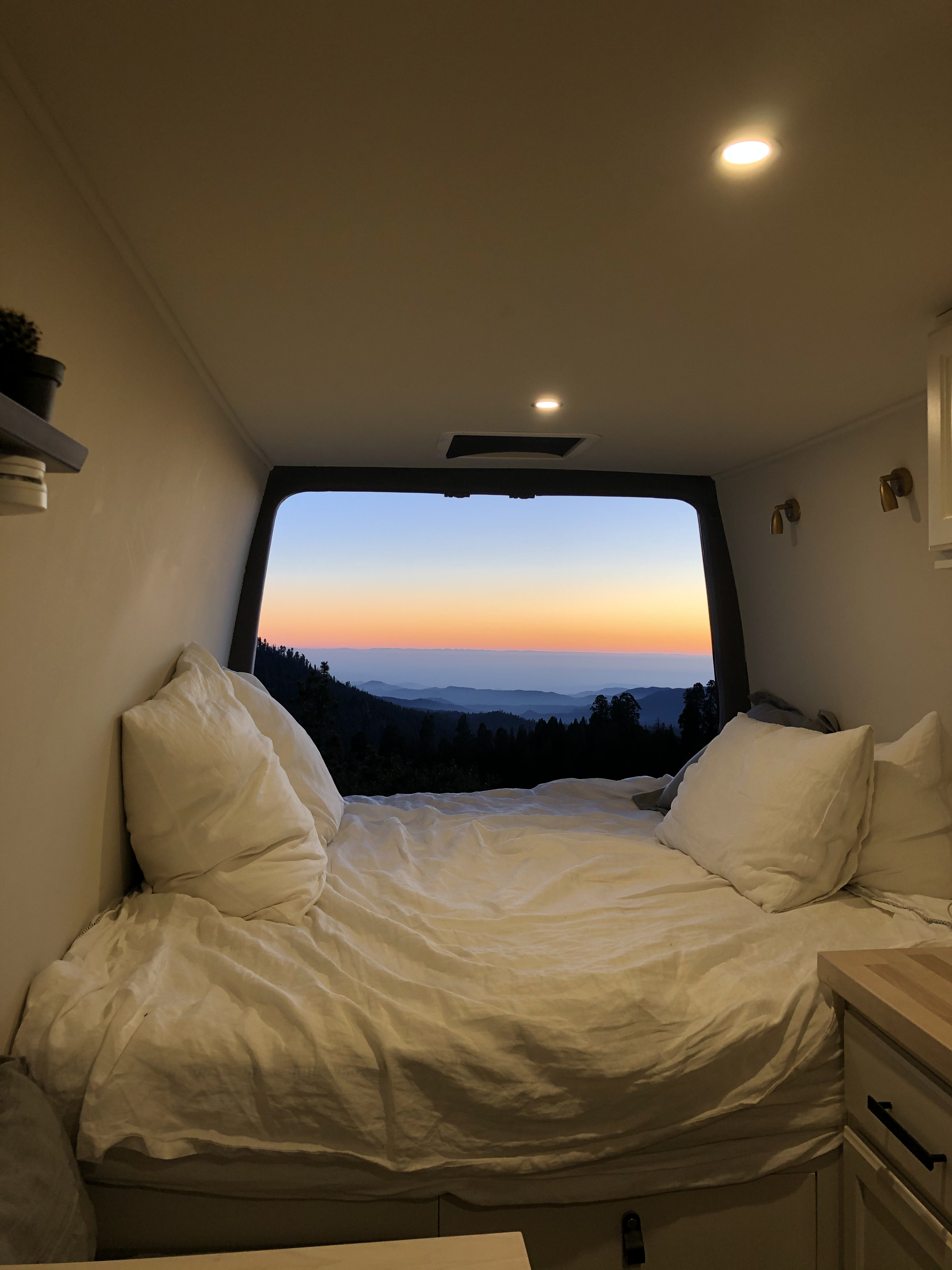 Cozy RV rental interior with a bed and stunning mountain sunset view. Perfect for van life adventures!. Dodge Sprinter 2008