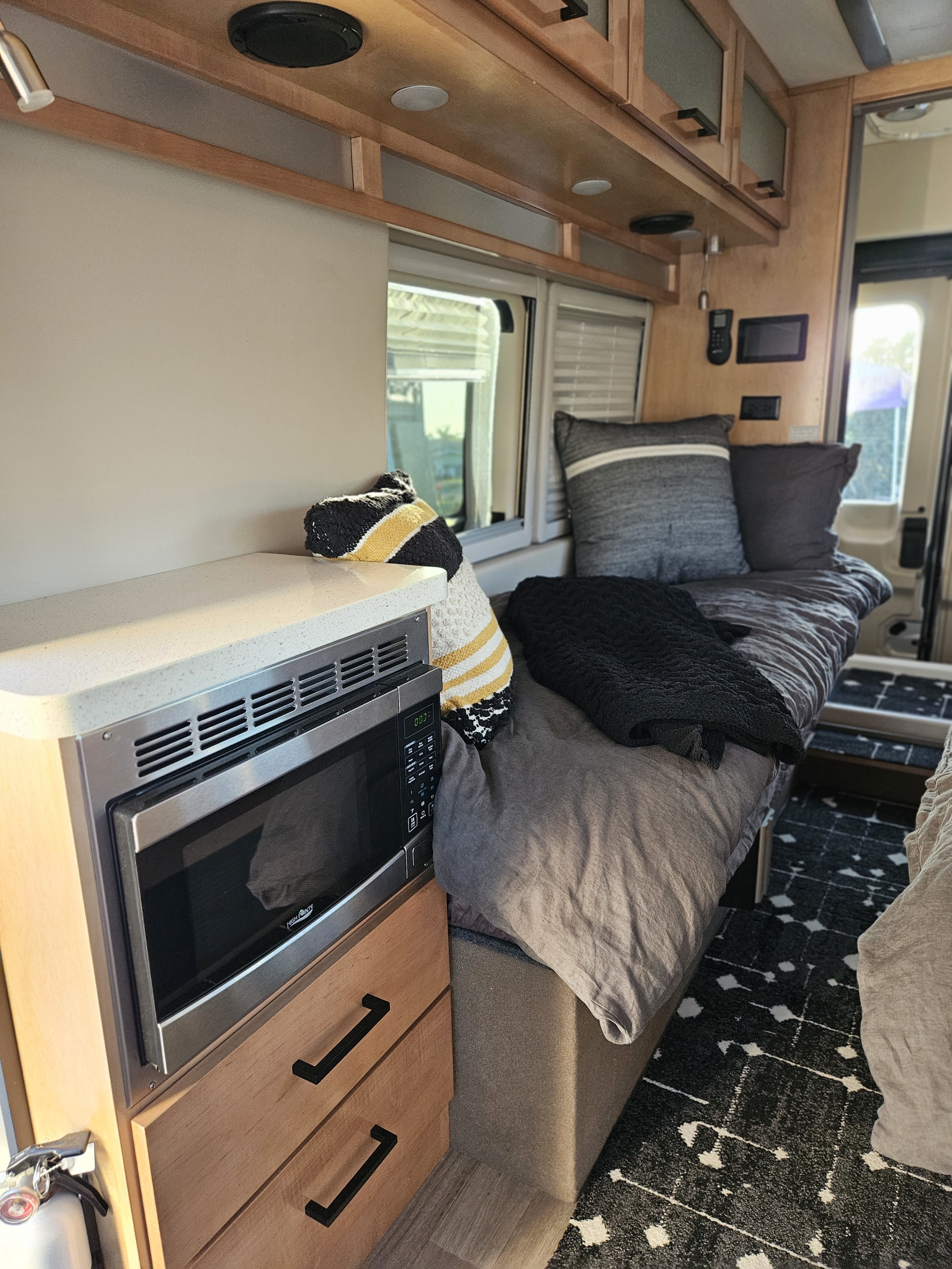 Inside a modern RV rental: microwave, countertop, comfy bed with pillows, wood accents, and patterned rug.. Forest River Coachmen Beyond 2023