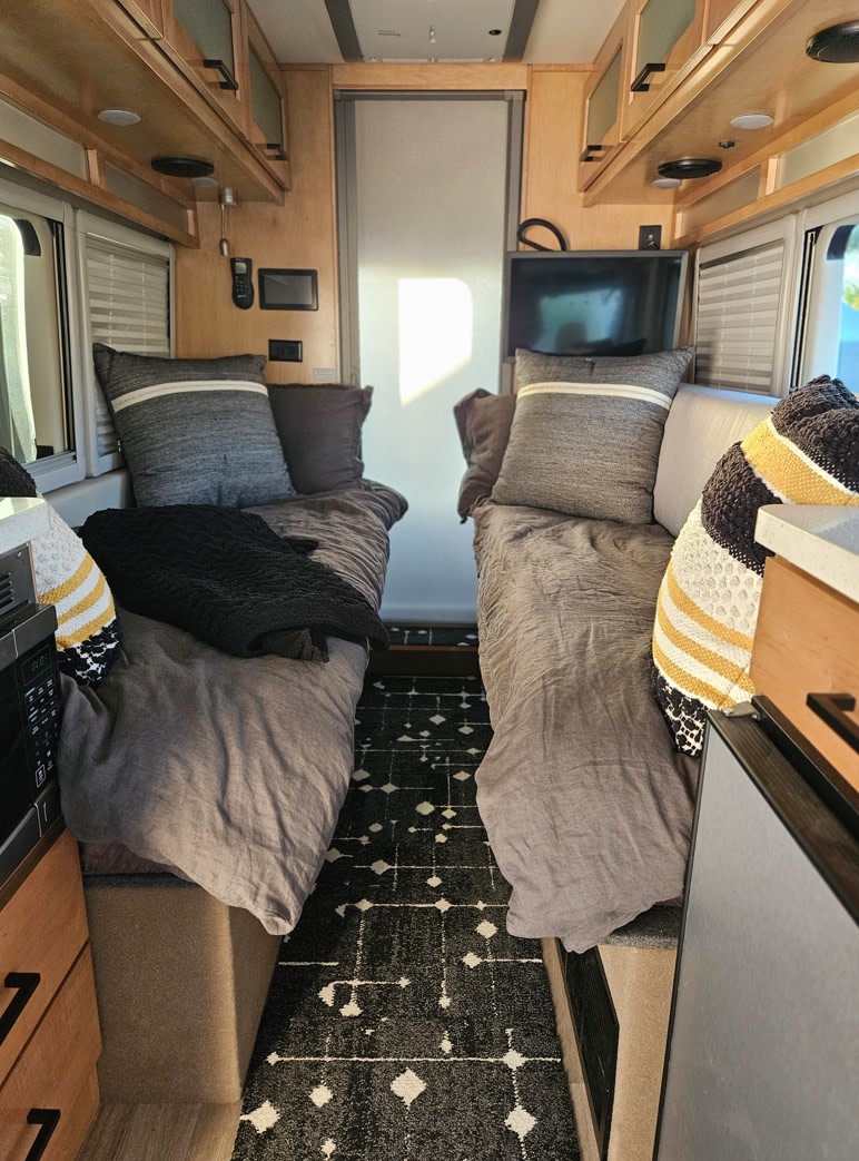 RV rental bedroom: Twin beds with grey linens, overhead storage, a TV, and a microwave in a compact, functional layout.. Forest River Coachmen Beyond 2023