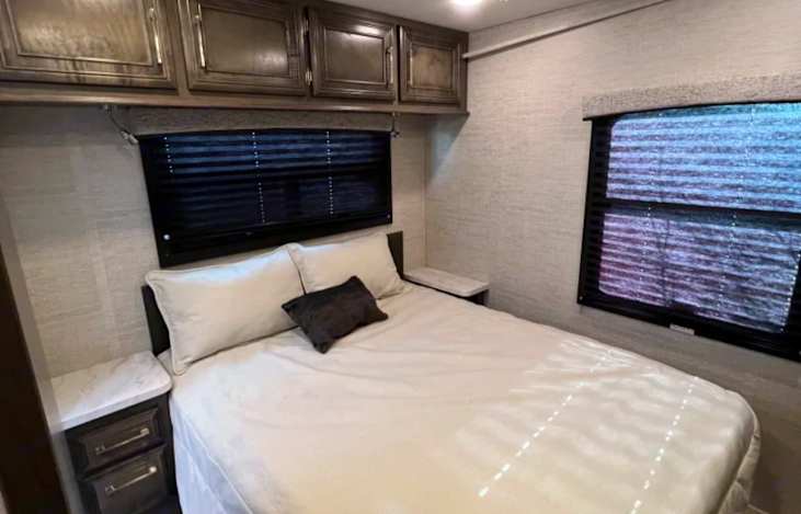 Step into comfort: This RV rental bedroom features a comfy bed, overhead cabinets, and bright windows.. Entegra Coach Odyssey 31F 2022