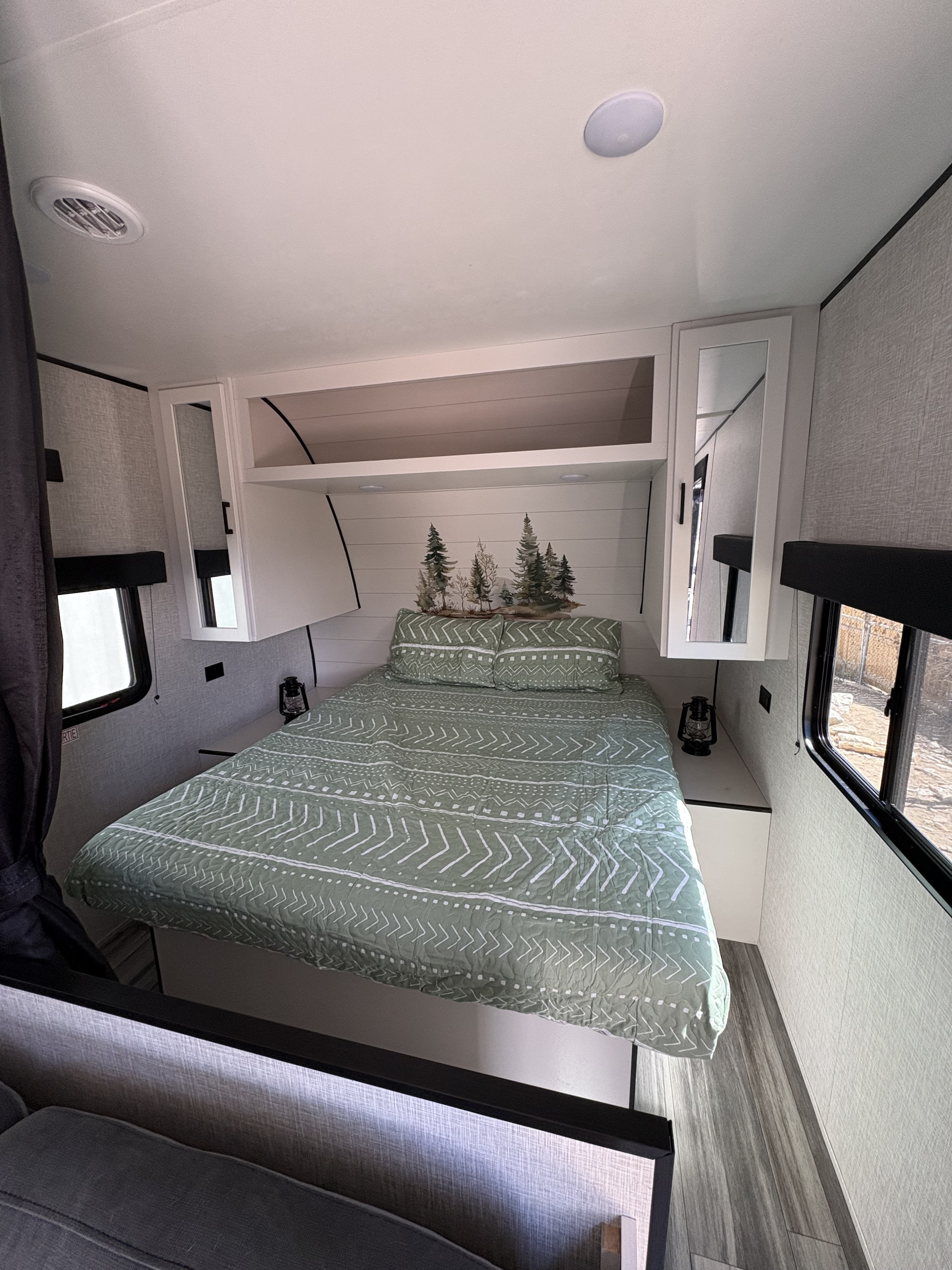 RV rental bedroom with a green patterned bed, forest wall art, white cabinets, and bright windows, offering a cozy space.. Jay Flight SLC 260BHW 2025