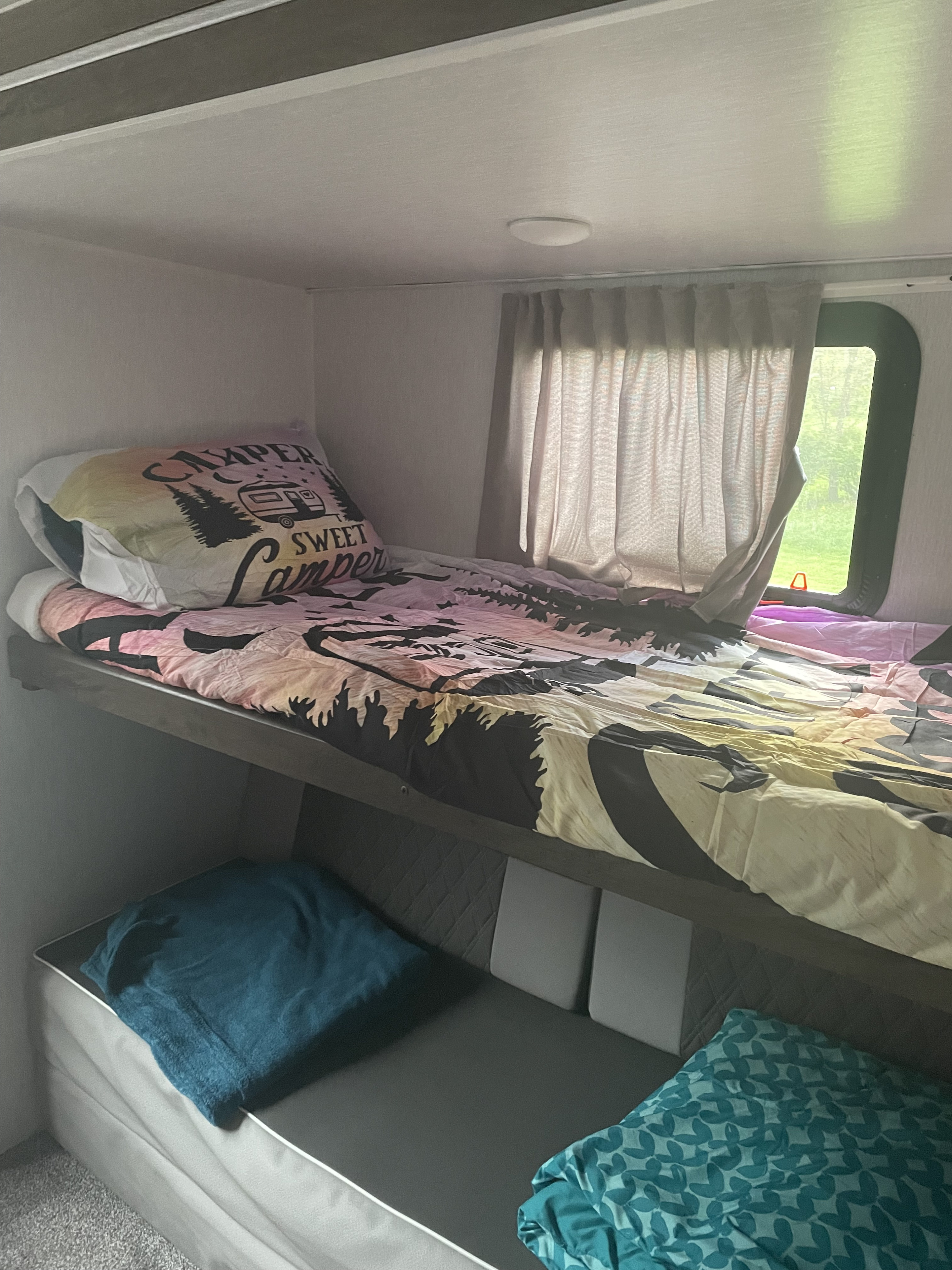 Inside an RV rental: a cozy bunk bed area with nature-themed bedding, curtains, and a window to nature.. Forest River Salem 2022
