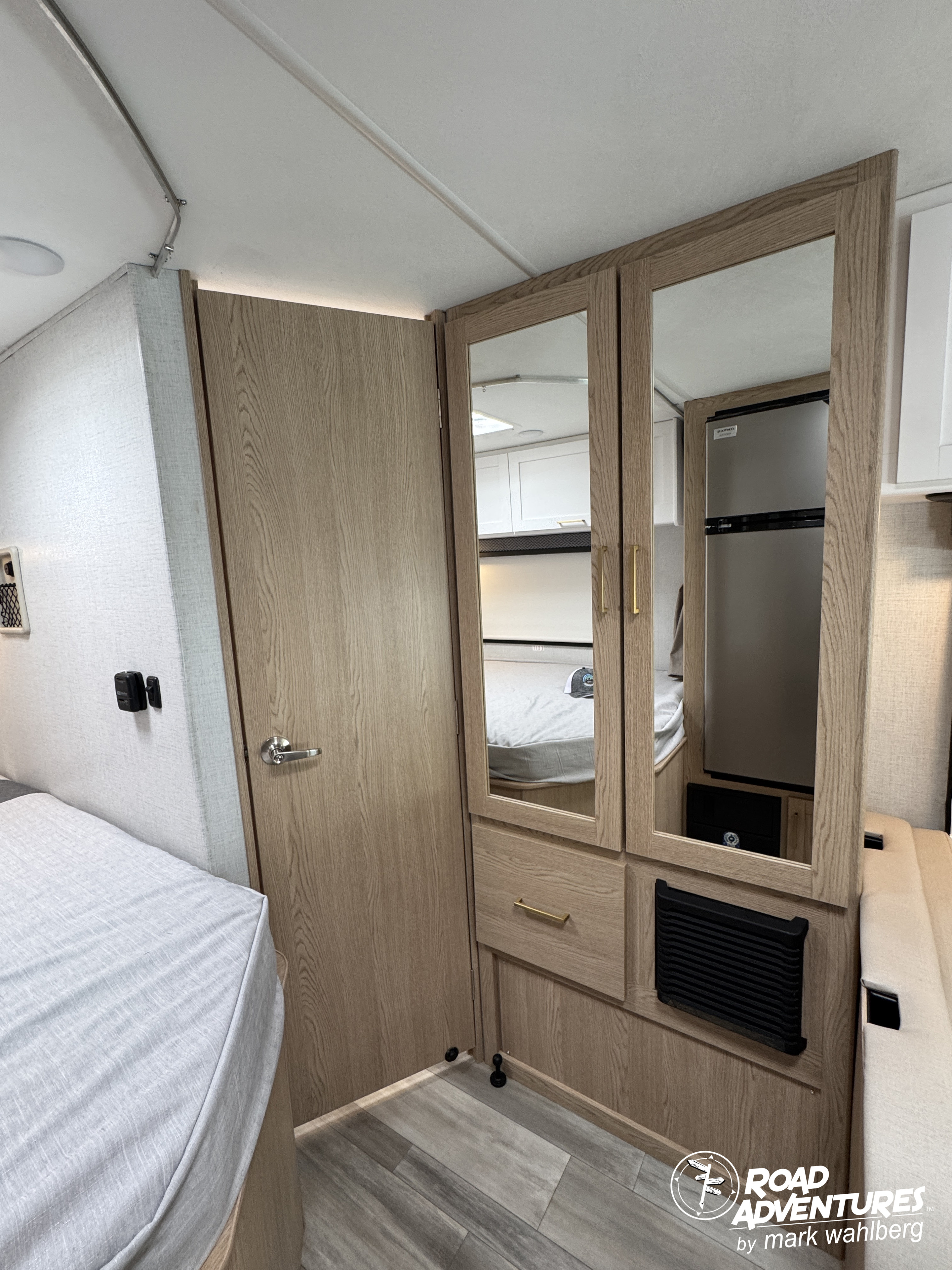 Compact RV rental interior featuring a bed, mirrored closet, door, and a reflected refrigerator. Ideal for travel.. Thor Motor Coach Four Winds 2026