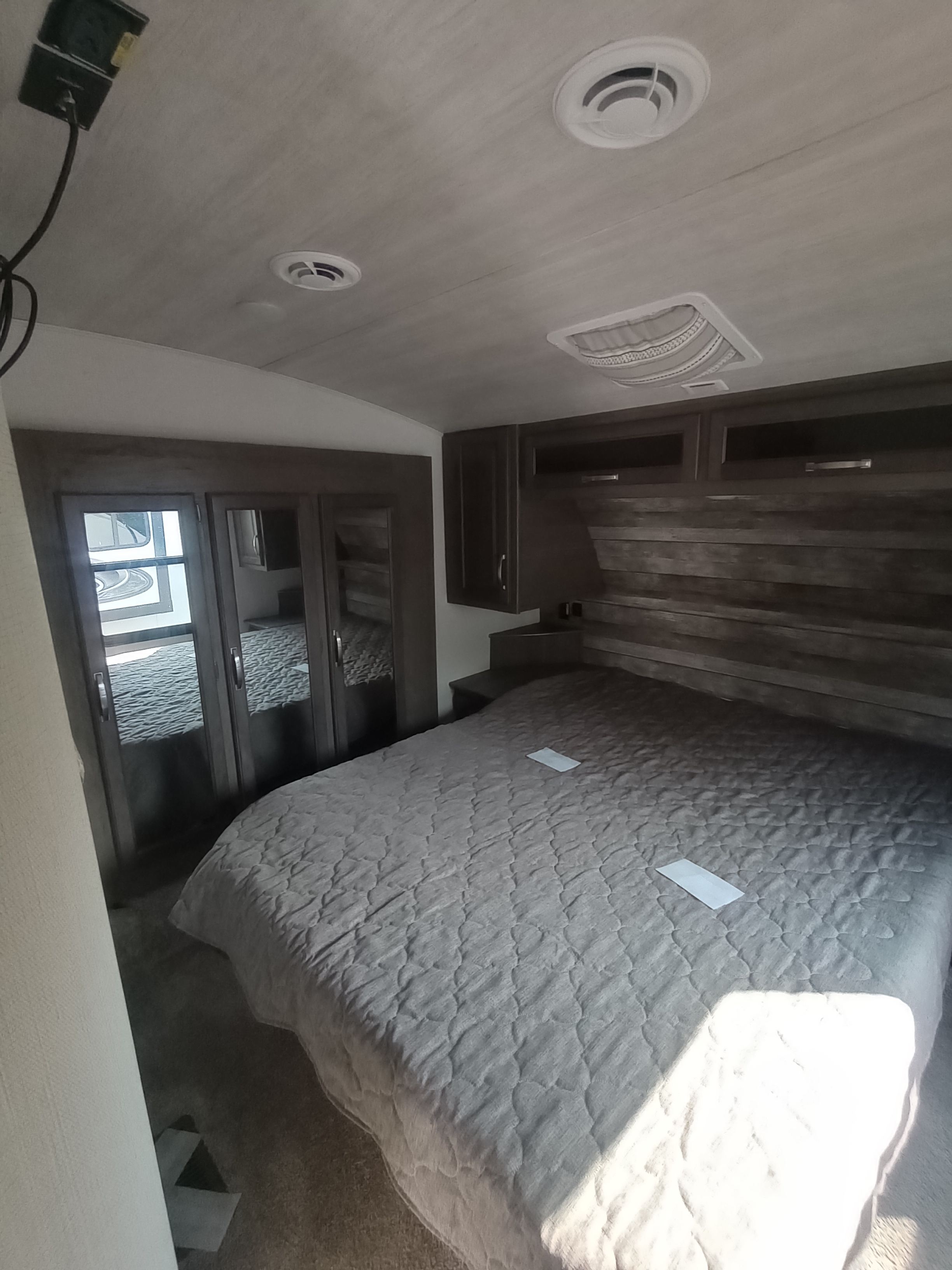 Inside an RV rental, a cozy bedroom featuring a large quilted bed, built-in wooden headboard, and mirrored closets.. Keystone RV Cougar 2022