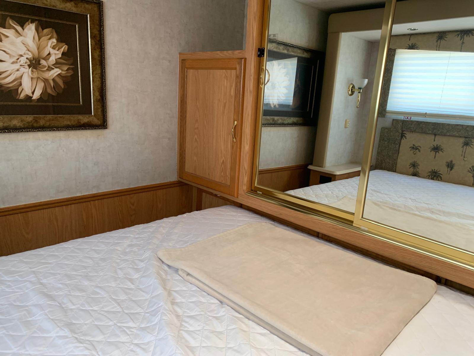 Comfortable RV rental bedroom with a quilted bed, mirrored closet, wooden cabinets, and framed floral art.. Ford DWR 2005