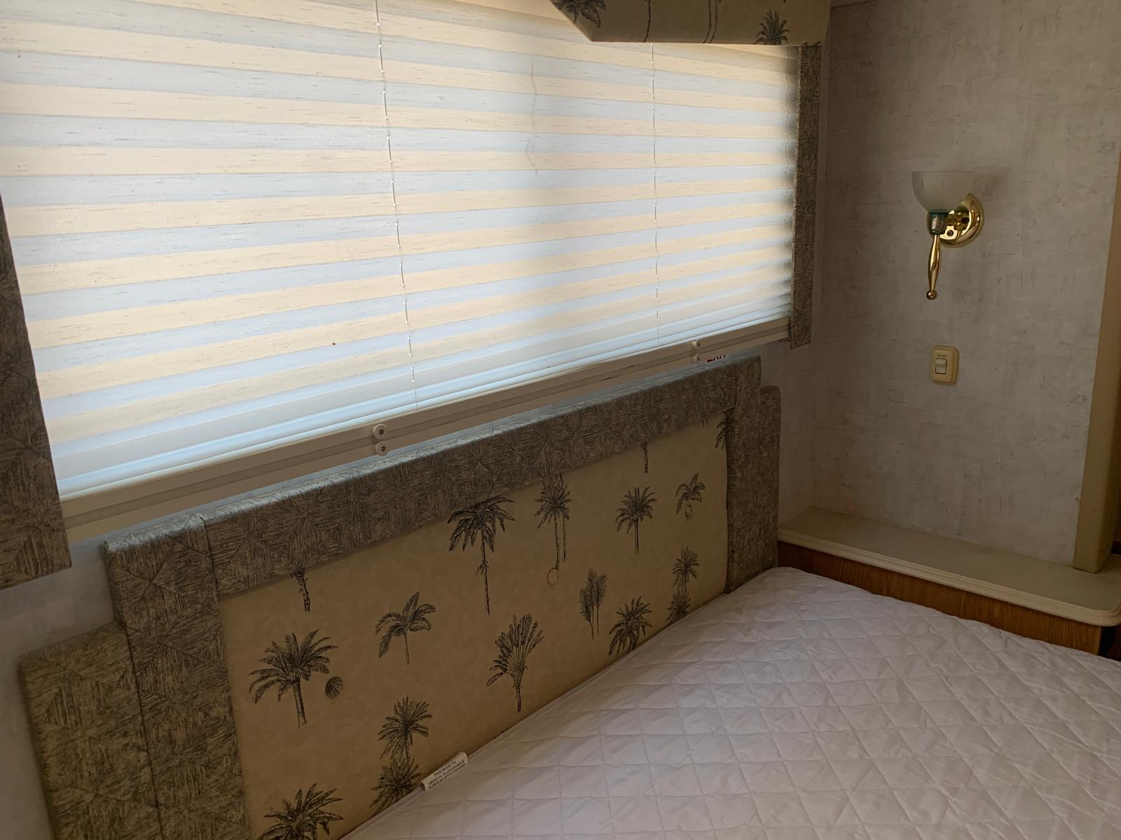 This RV rental bedroom features a bed with a white quilted mattress pad, palm tree headboard, and striped window blinds.. Ford DWR 2005