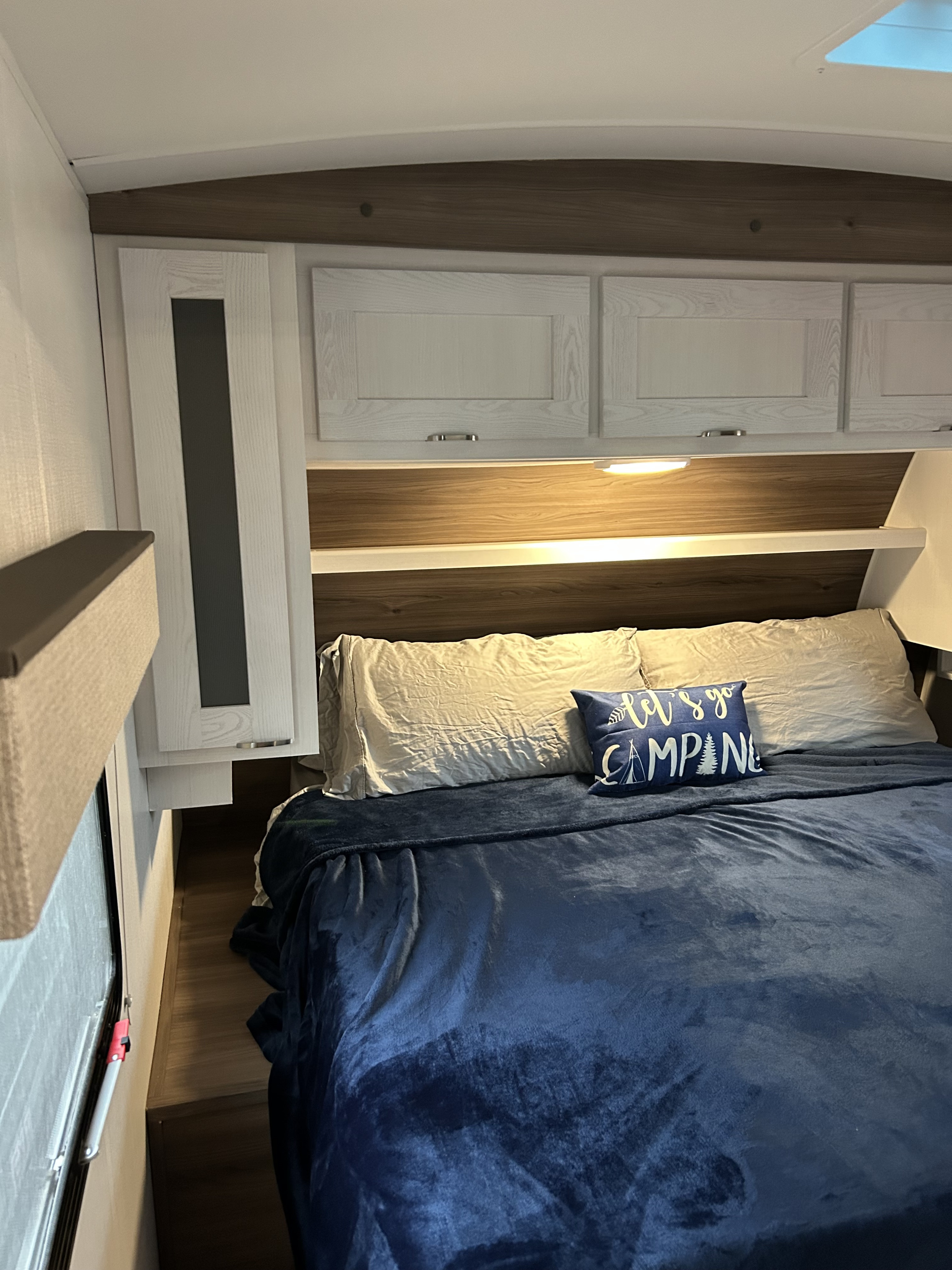 Cozy RV rental bedroom with blue blanket, pillows, overhead cabinets, and a 'Let's Go Camping' pillow.. MPG 3100BH 2025