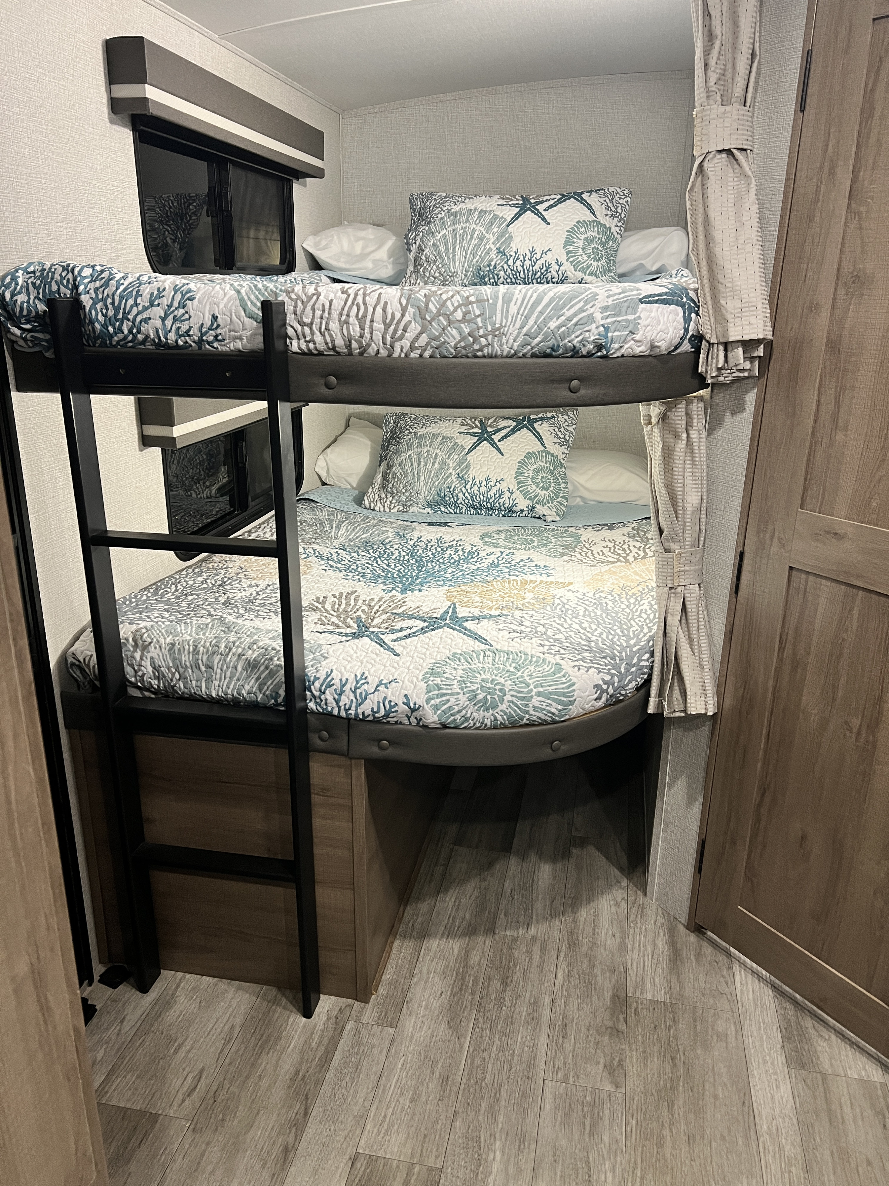 Cozy RV rental bunk beds with marine-themed bedding, featuring a ladder and storage, offer comfortable sleep.. Grand Design Imagine 2023