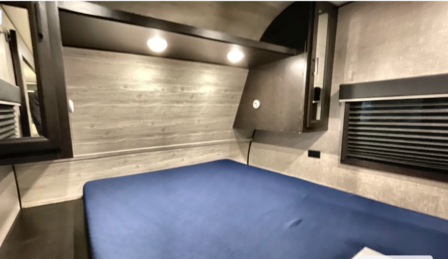 RV rental bedroom interior: blue bed, overhead reading lights, mirrored cabinet, storage, and window with blinds.. Jayco Jay Flight SLX 2022