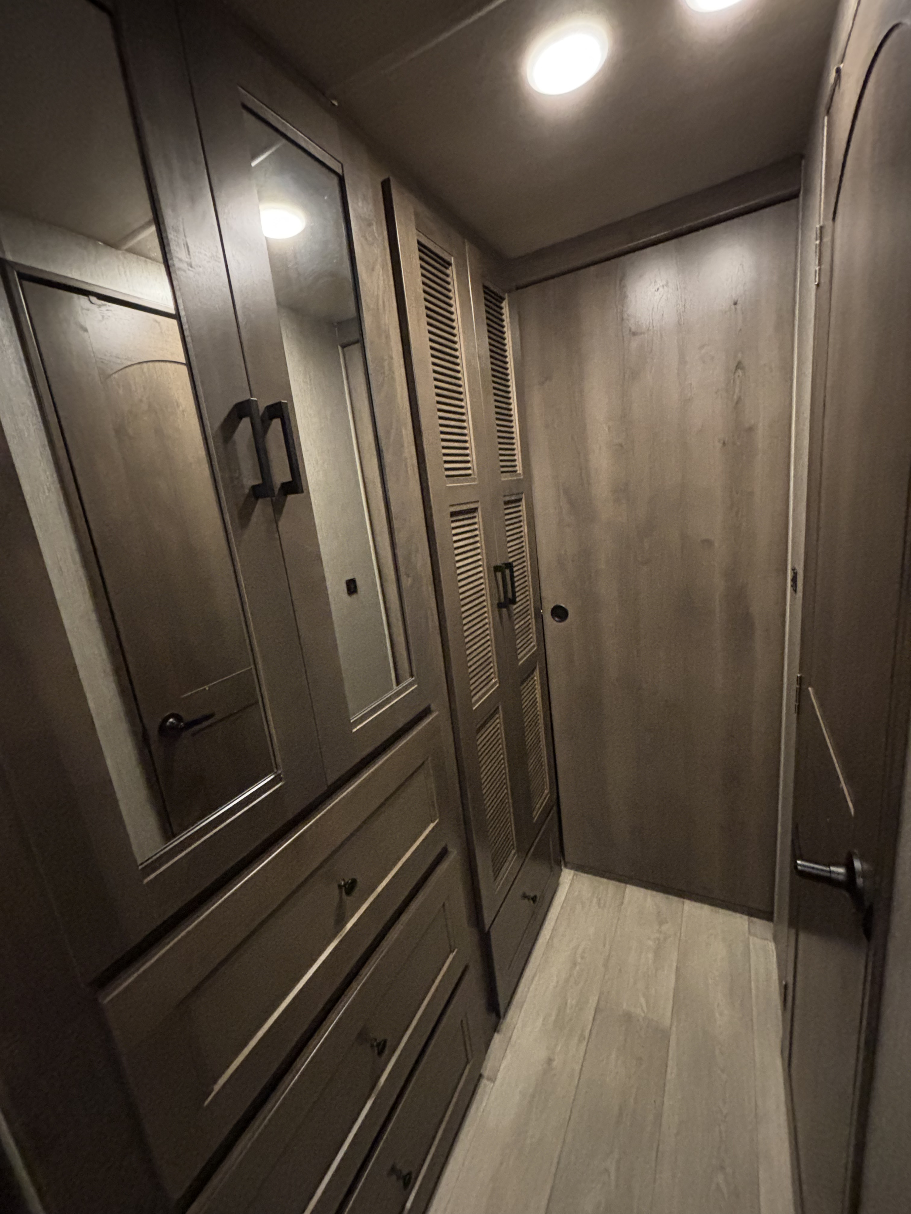 RV rental: Modern, compact interior hallway with dark wood-toned mirrored and louvered storage cabinets, and a light wood-look floor.. Nexus RV Triumph Super C 2023
