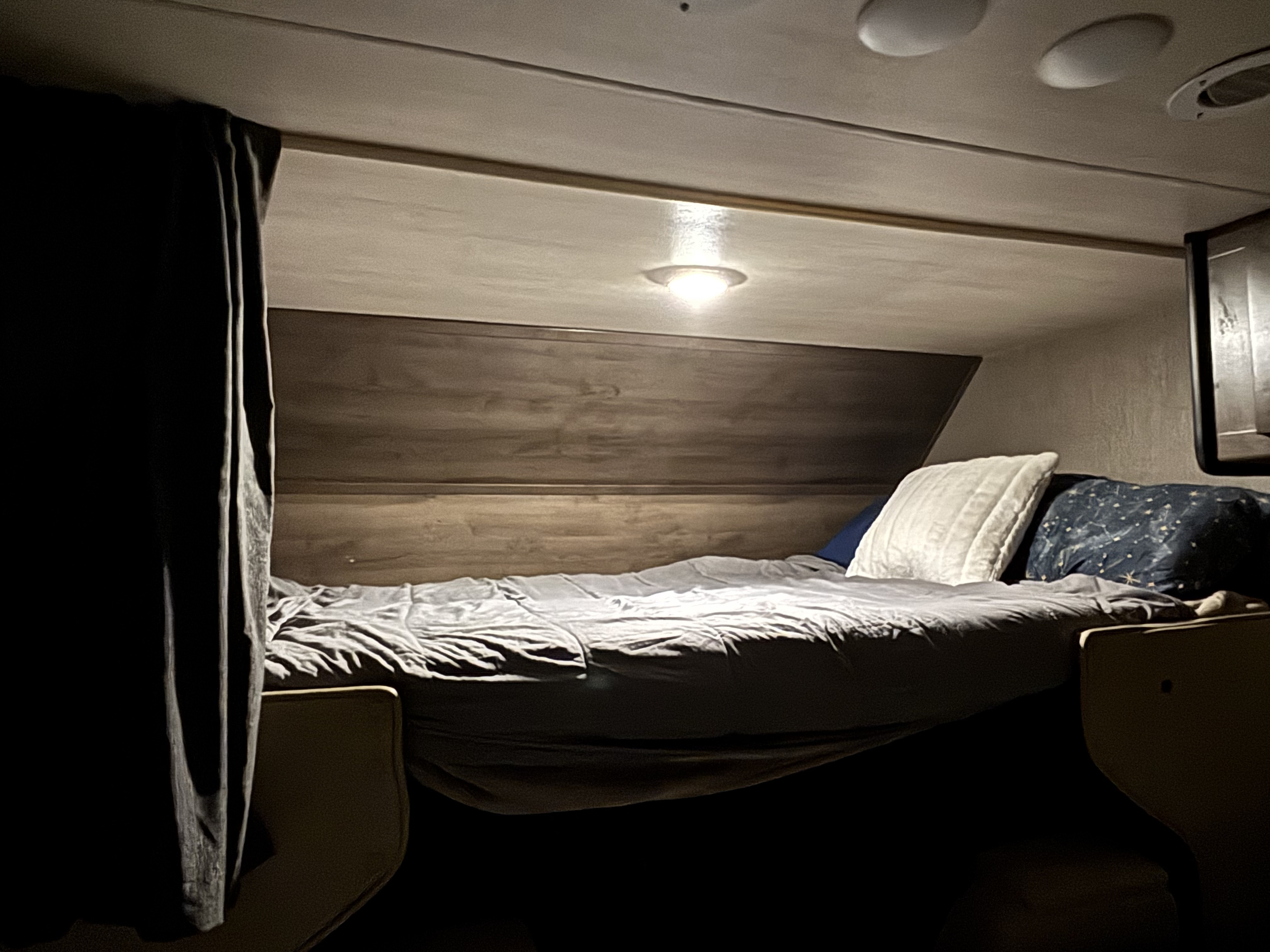 An inviting RV rental sleeping area features a made bed, headboard, and soft light, perfect for cozy travel.. Nexus RV Triumph Super C 2023