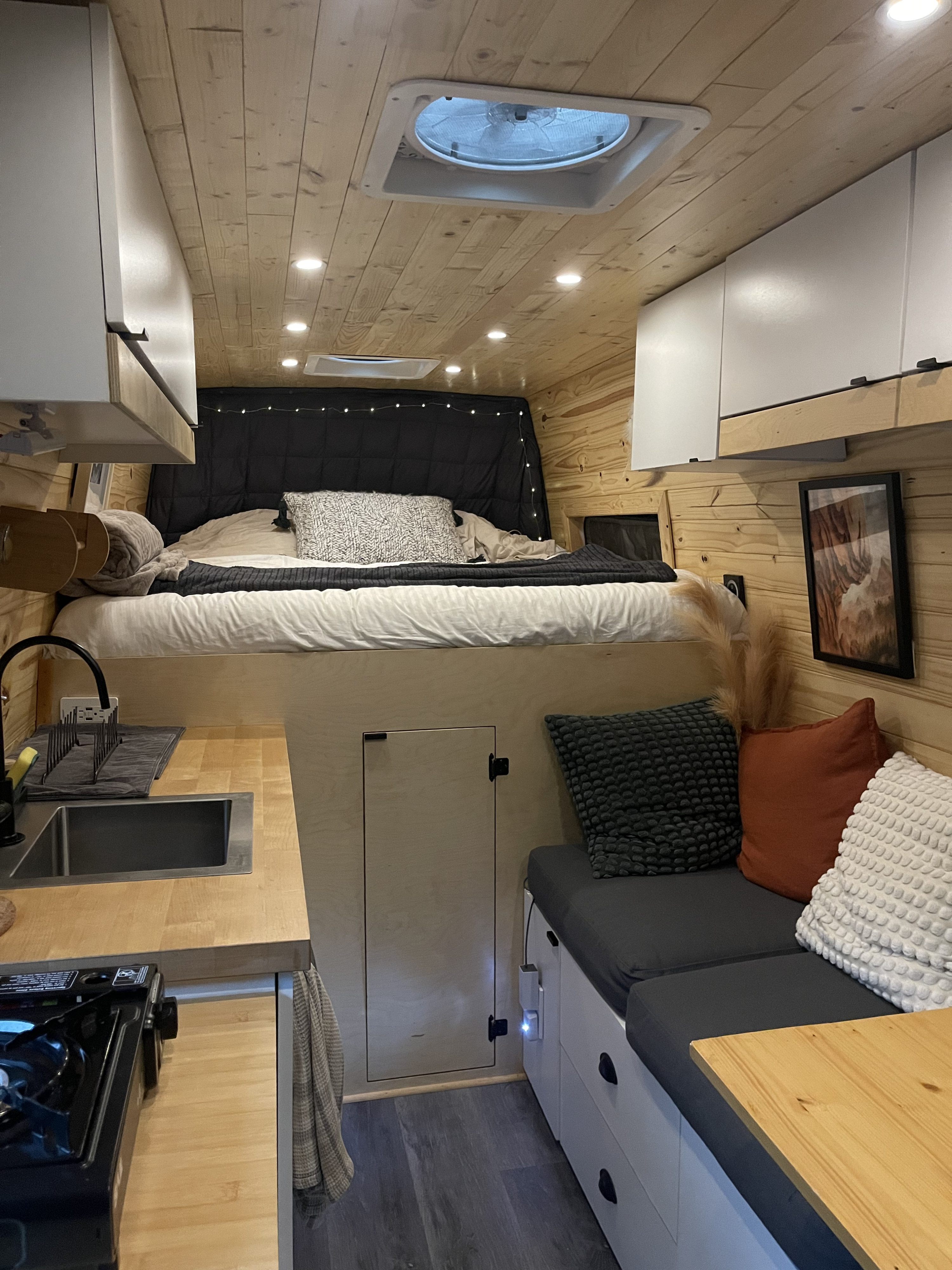 Inside a stylish RV rental, showcasing a raised bed, compact kitchenette, and comfy lounge area with storage.. Mercedes-Benz Sprinter 2012