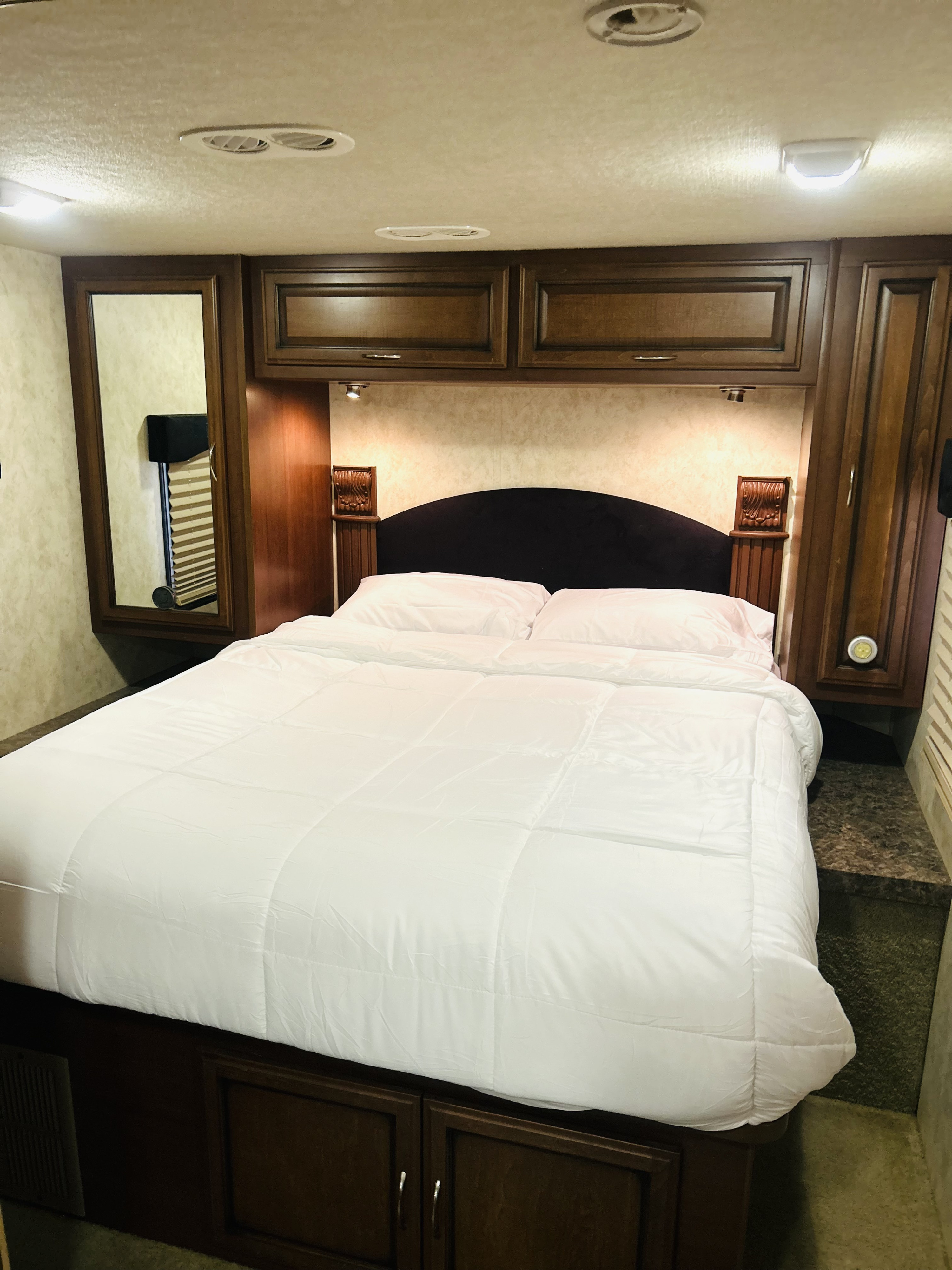Bright RV rental bedroom featuring a comfy bed with white bedding, dark wood cabinets, and a mirror.. Fleetwood Storm 2011