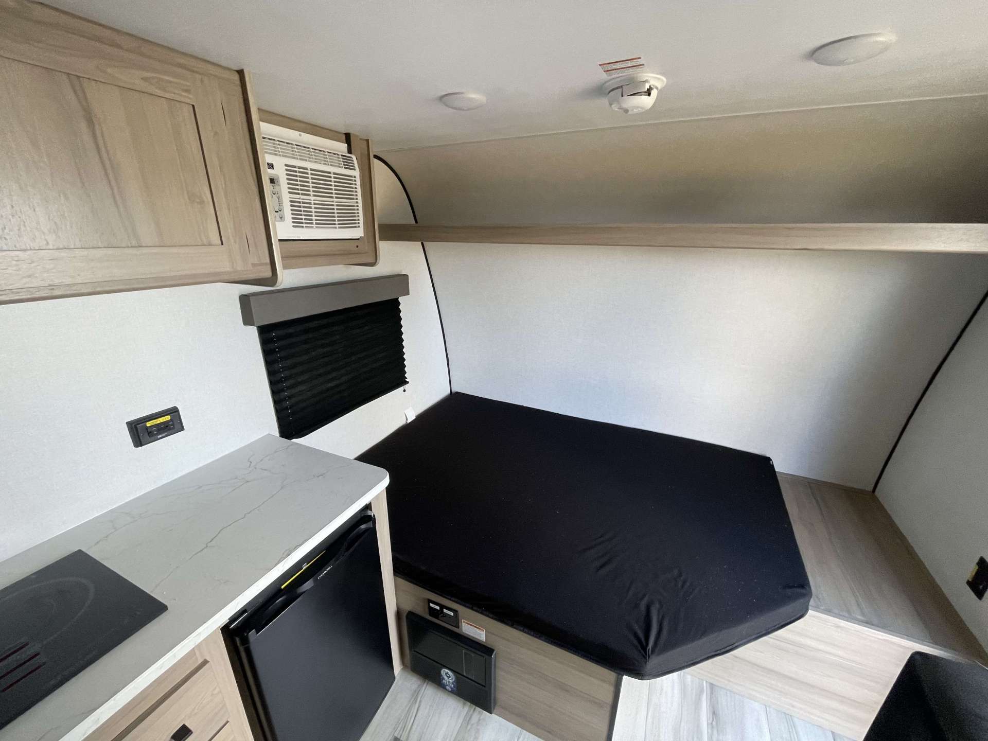 RV rental interior features a cozy bed, compact kitchen with fridge, and AC. Perfect for adventurers.. Keystone RV Coleman 13B 2025