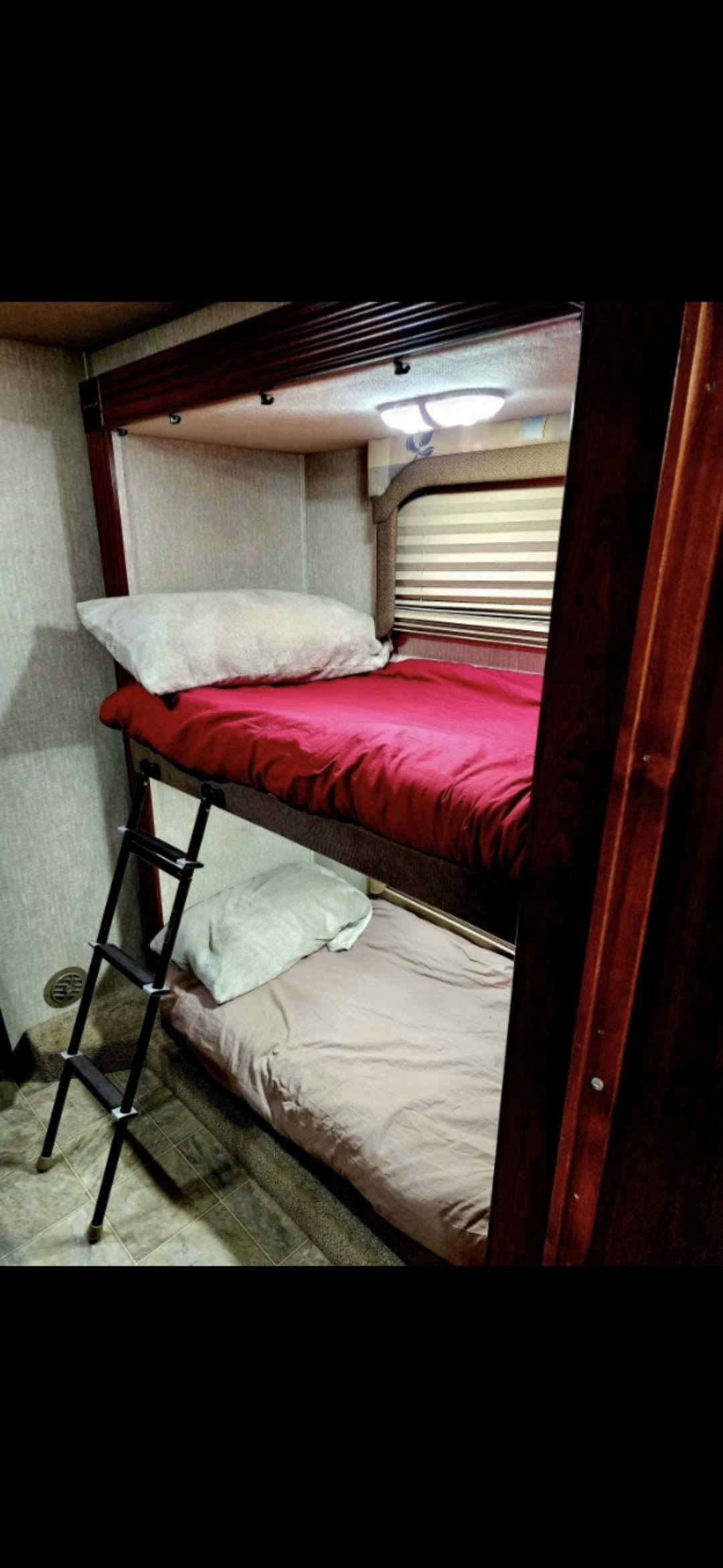 Cozy RV rental bunk beds with ladder, red and beige bedding, and window. Ideal for compact sleeping in your travel trailer.. Fleetwood Fiesta LX 2008