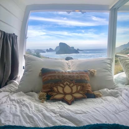 An RV rental bed overlooks a stunning ocean view through a large window, featuring sea stacks & blue sky.. Mercedes-Benz sprinter 2019