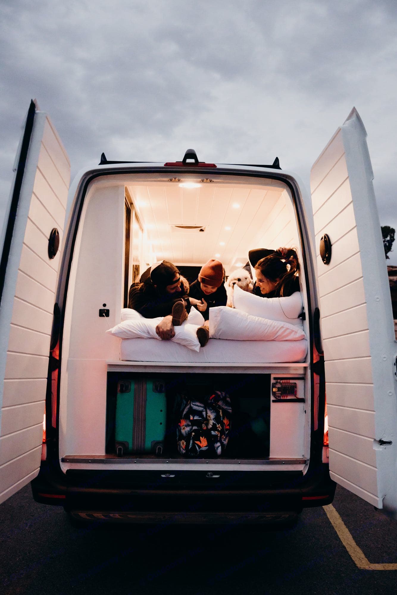 Experience RV rental: A family & dog enjoy a cozy, brightly lit camper van interior, with open back doors.. Mercedes-Benz sprinter 2019