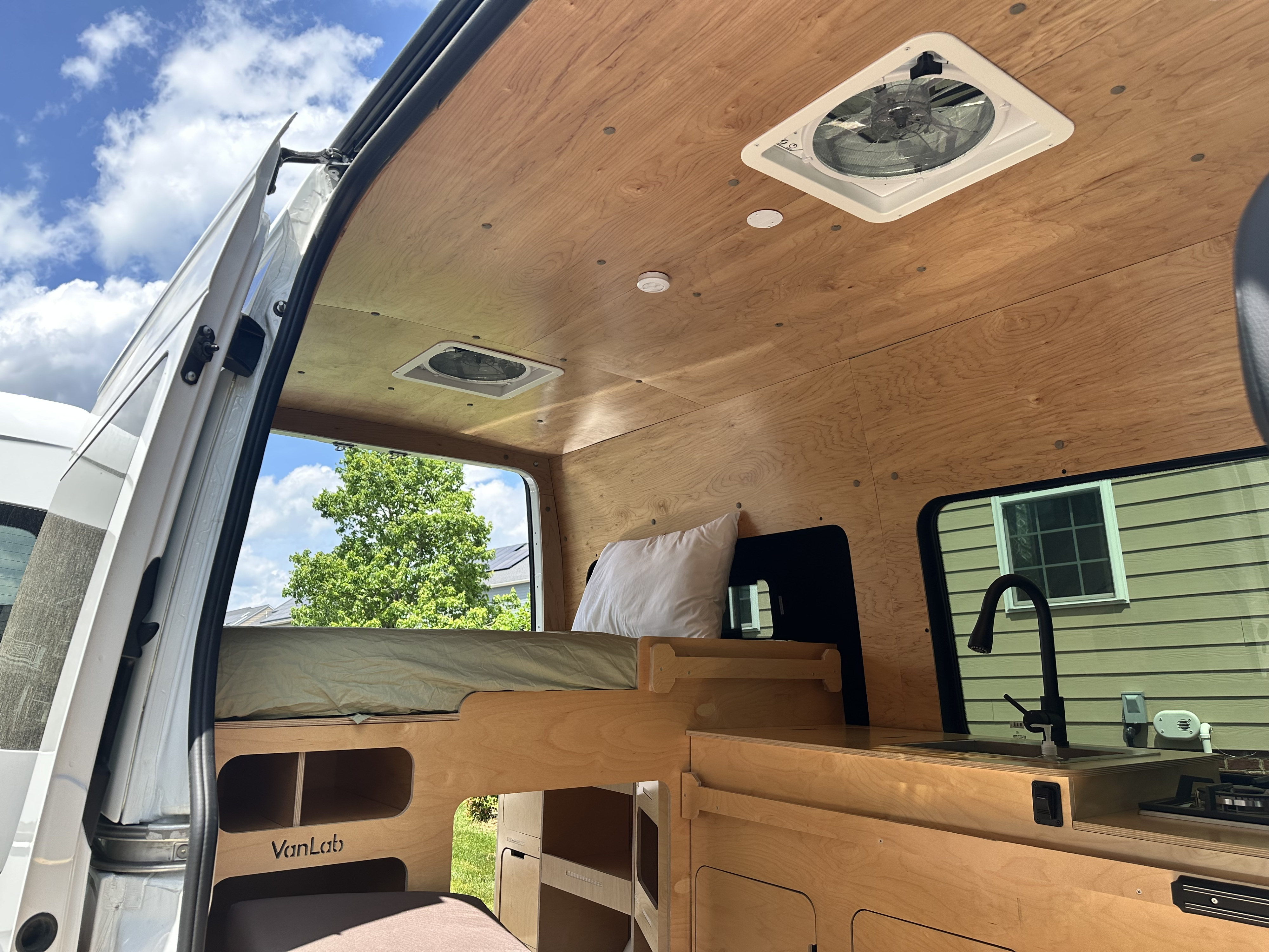 VanLab rv rental interior: wood-paneled, with a comfortable bed, kitchenette featuring a sink, and ceiling fans.. Mercedes-Benz Sprinter 2021