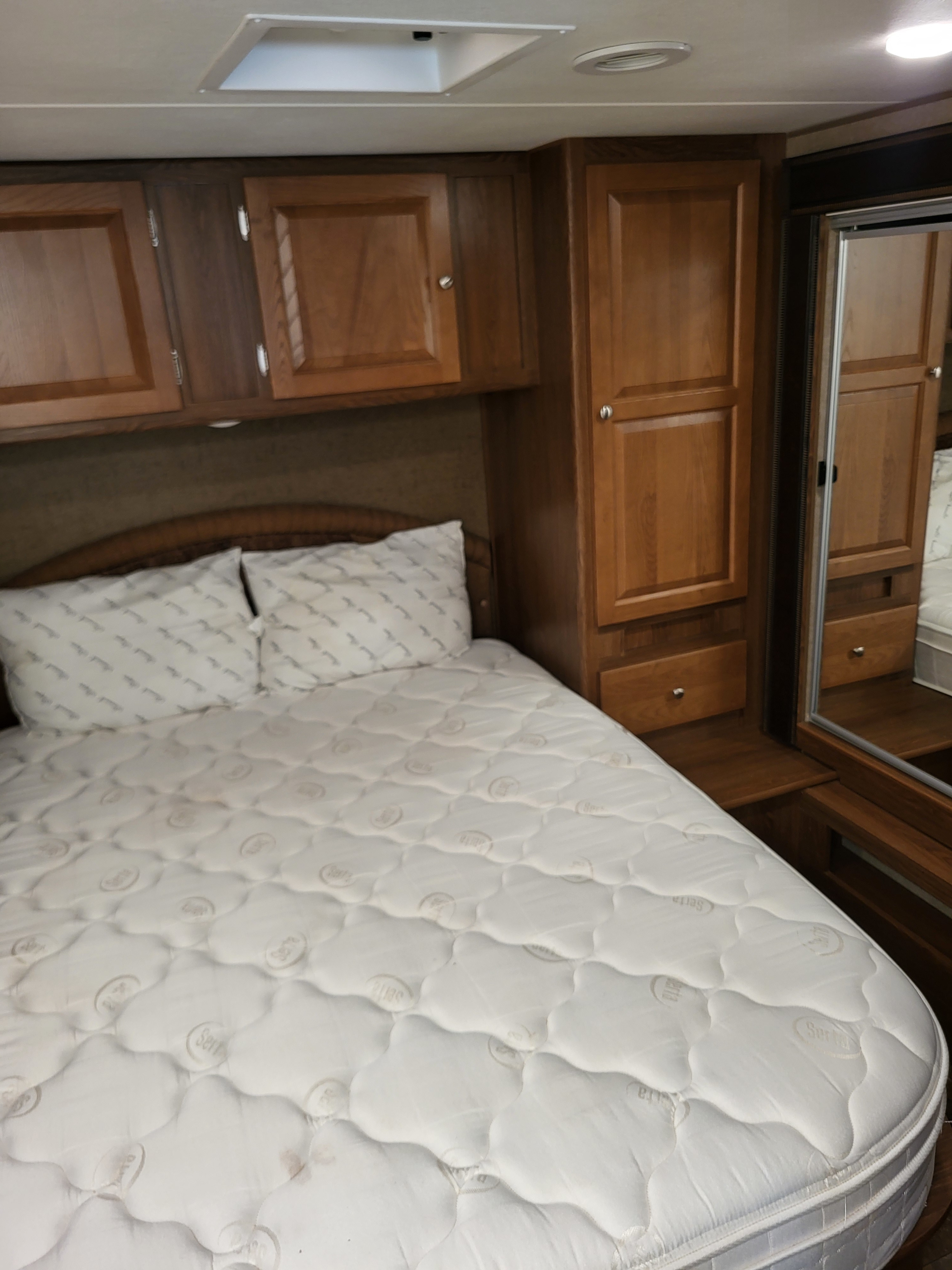 RV rental bedroom: cozy bed, overhead cabinets, and built-in mirrored wardrobe for compact comfort.. Coachmen Leprechaun 2016