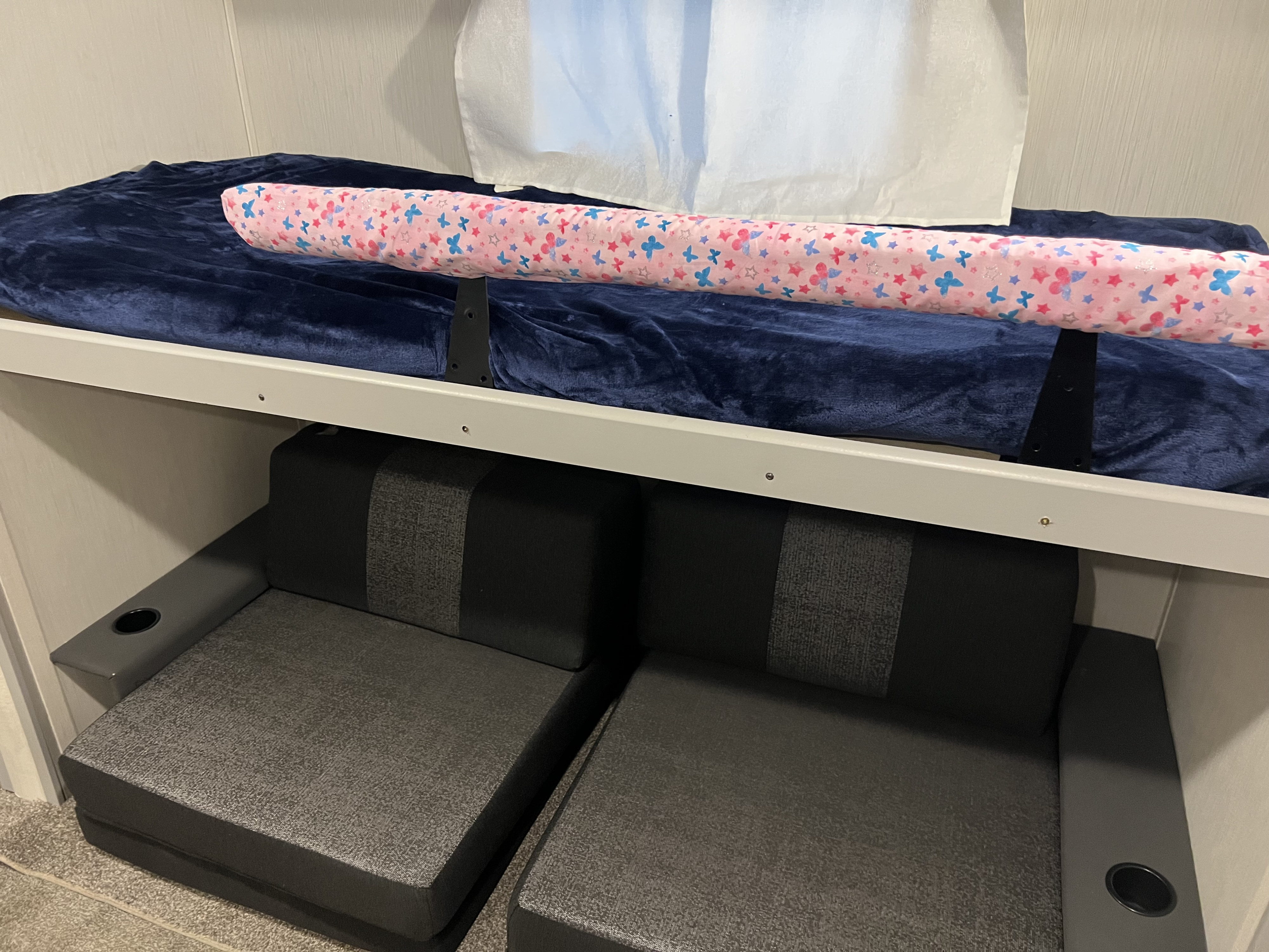 RV rental bunk bed with soft blue blanket and decorative pillow, above modular sofas featuring a cup holder.. Forrest River Vibe 2022