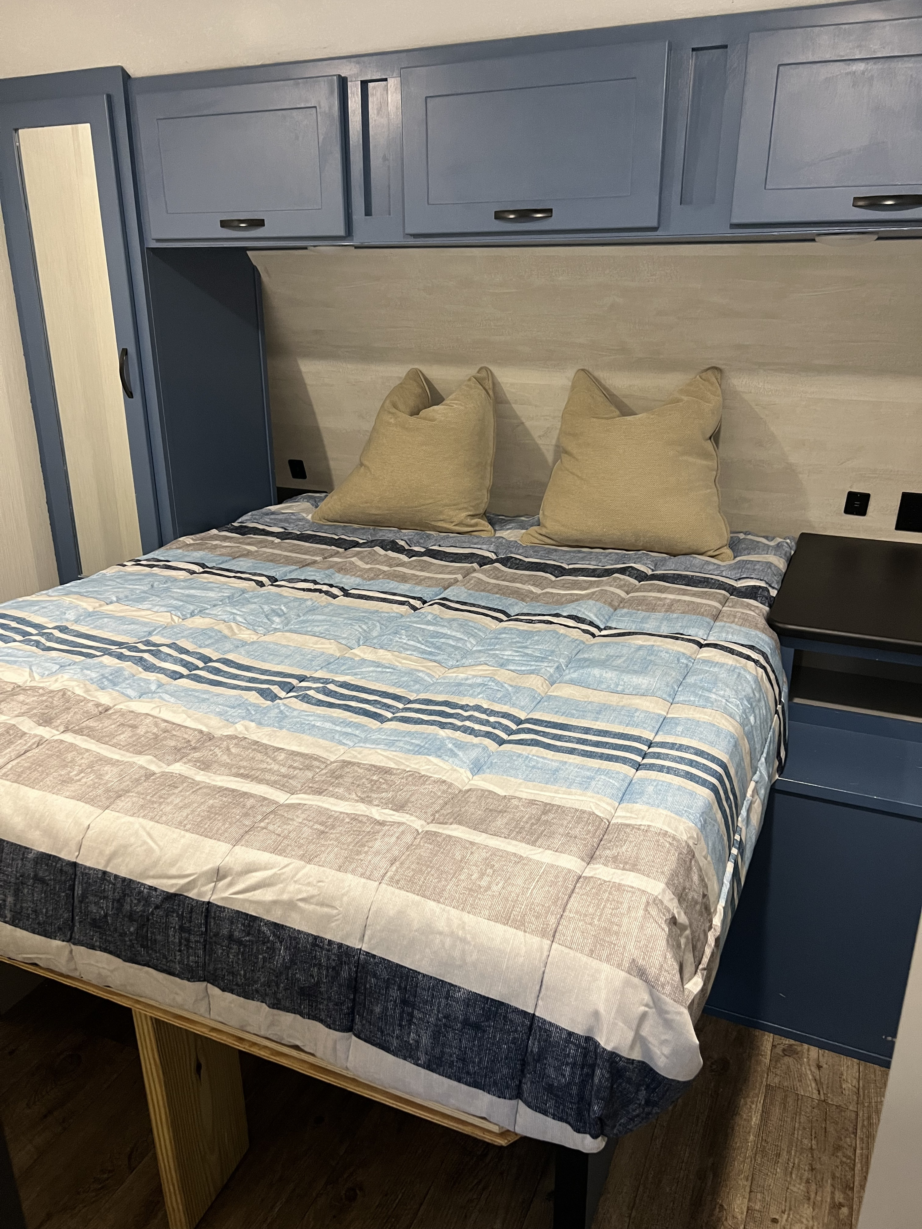 Cozy RV rental bedroom with blue cabinets, striped bedding, and built-in nightstand. Perfect camper comfort.. Forrest River Vibe 2022
