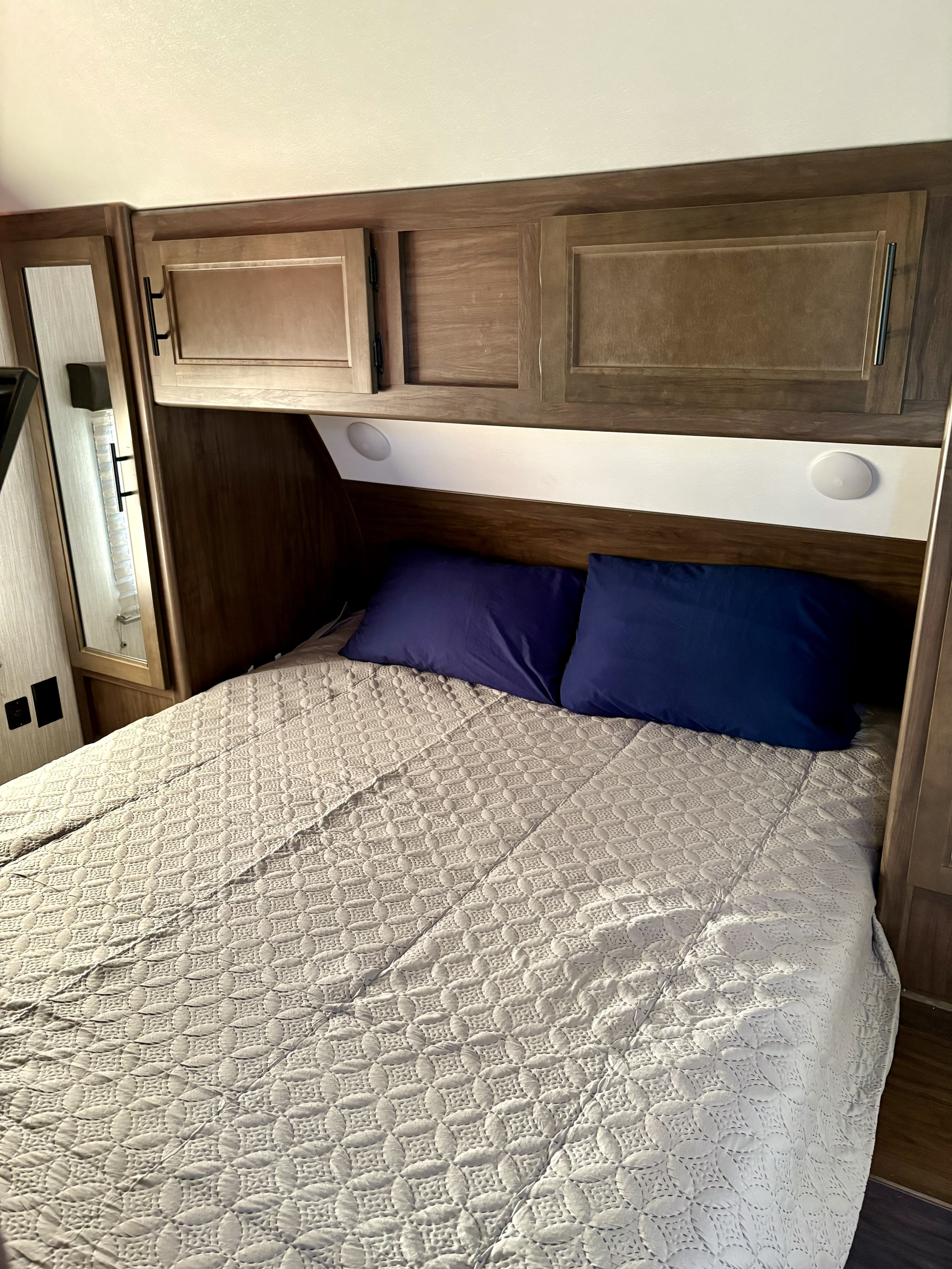 Cozy RV rental bedroom with a patterned comforter, blue pillows, and wooden overhead storage.. Forest River Cherokee Grey Wolf 2021