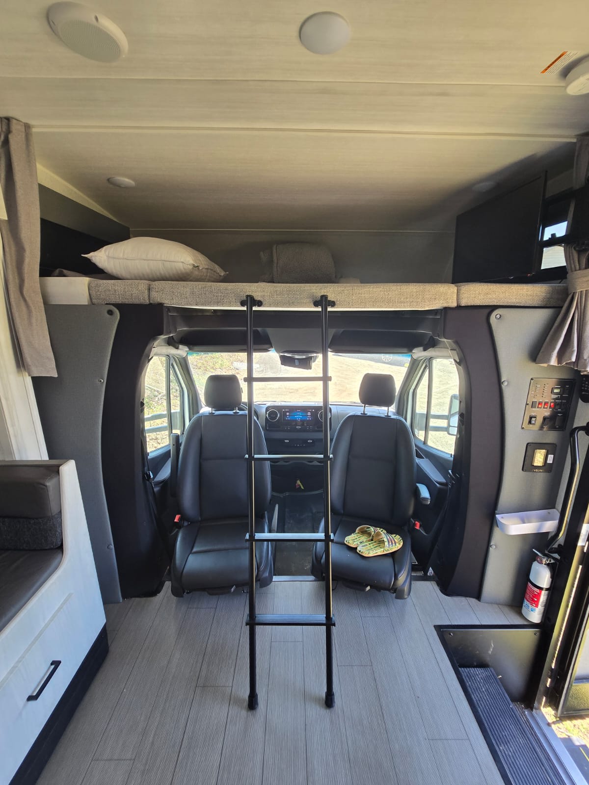 Spacious RV rental interior: front cockpit, overhead bunk with ladder, and side seating. Modern, ready for your next trip.. EAST TO WEST Entrada M-Class 2023