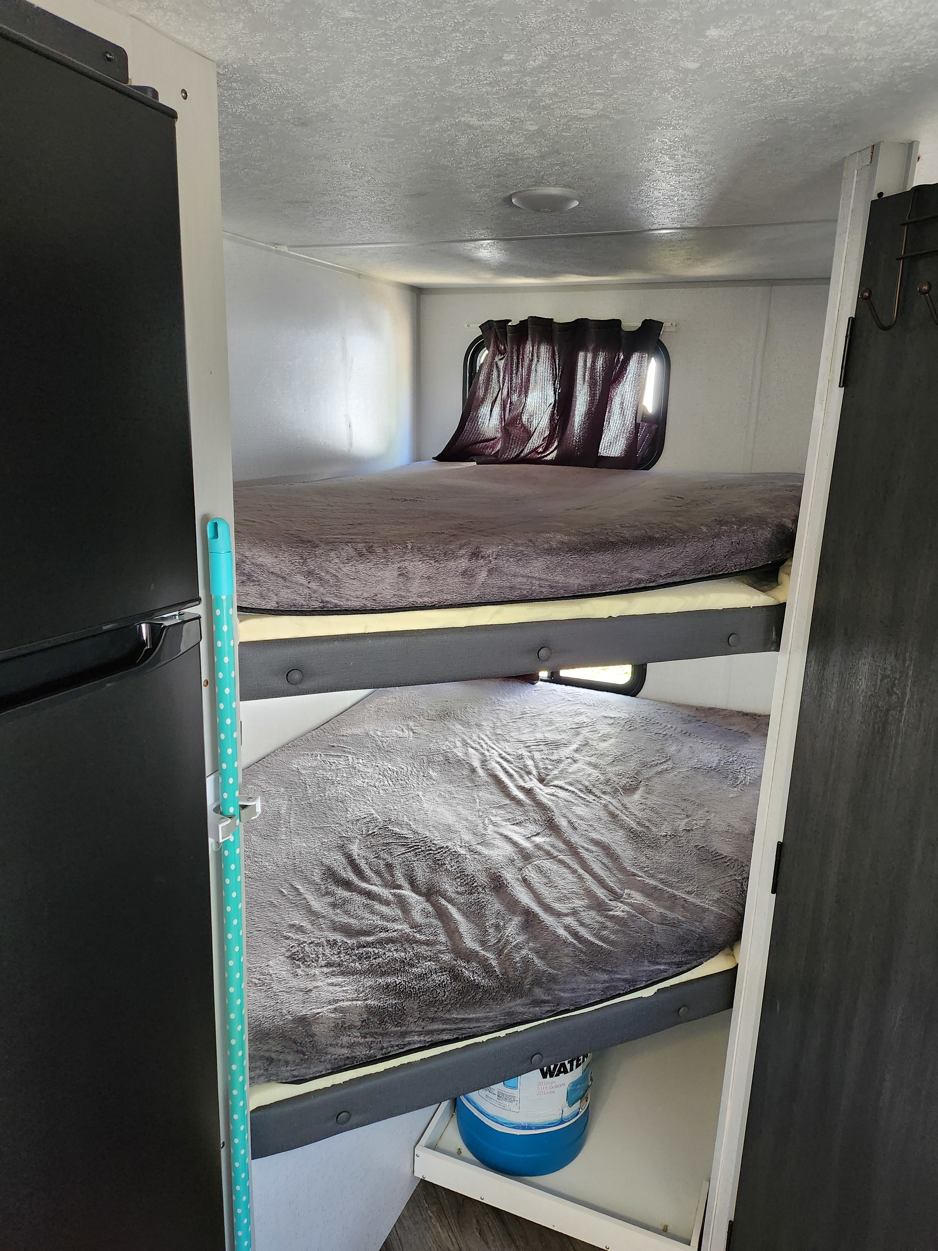 Inside an RV rental: stacked bunk beds with soft blankets, small windows, a refrigerator, and essential water storage visible.. Forest River Wildwood FSX 2022