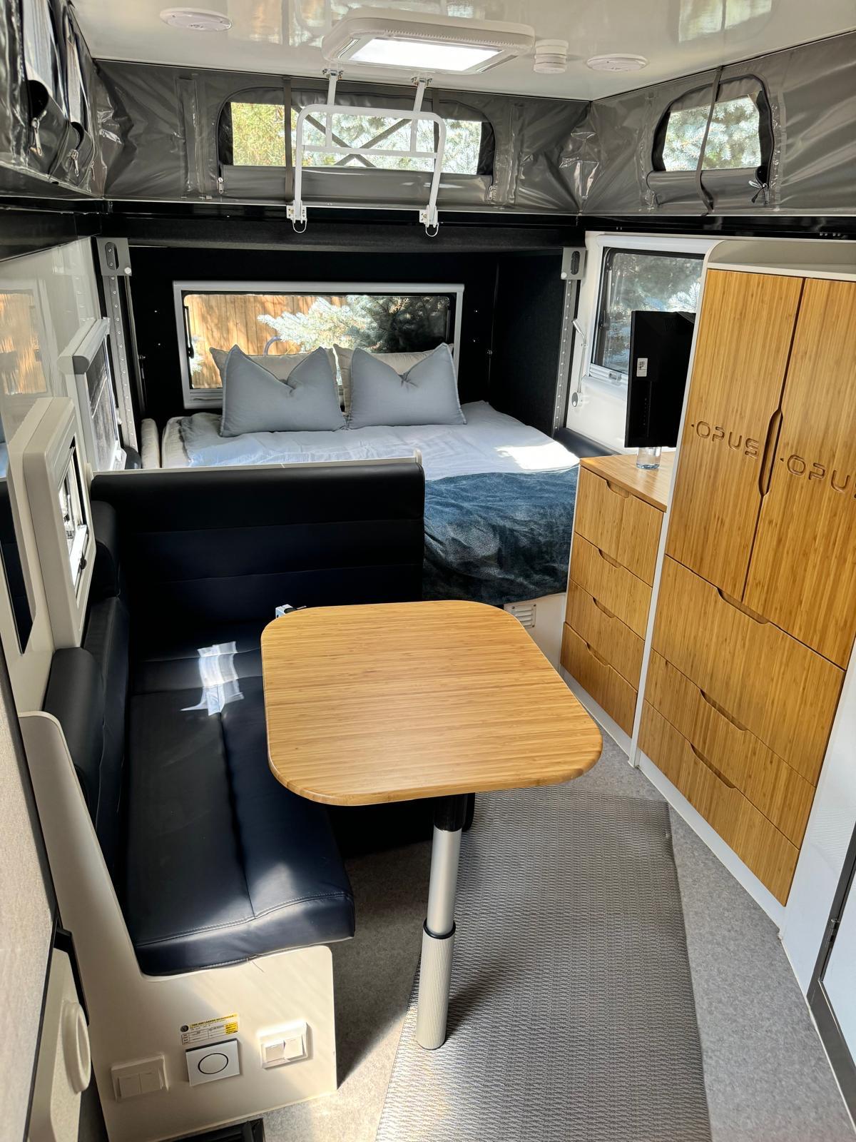 Experience comfort in this RV rental. Features include a rear bed, dining area with black bench, and bamboo storage.. Opus OP15 2020