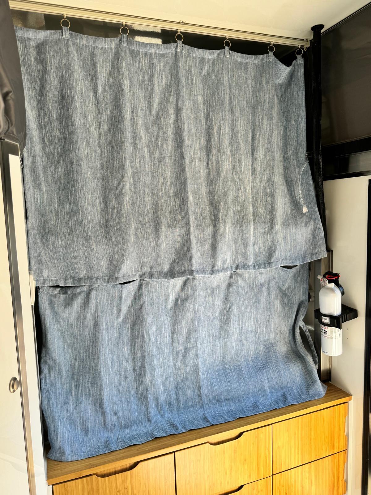 Light blue privacy curtains inside an RV rental, with bamboo drawers below and a fire extinguisher mounted for safety.. Opus OP15 2020