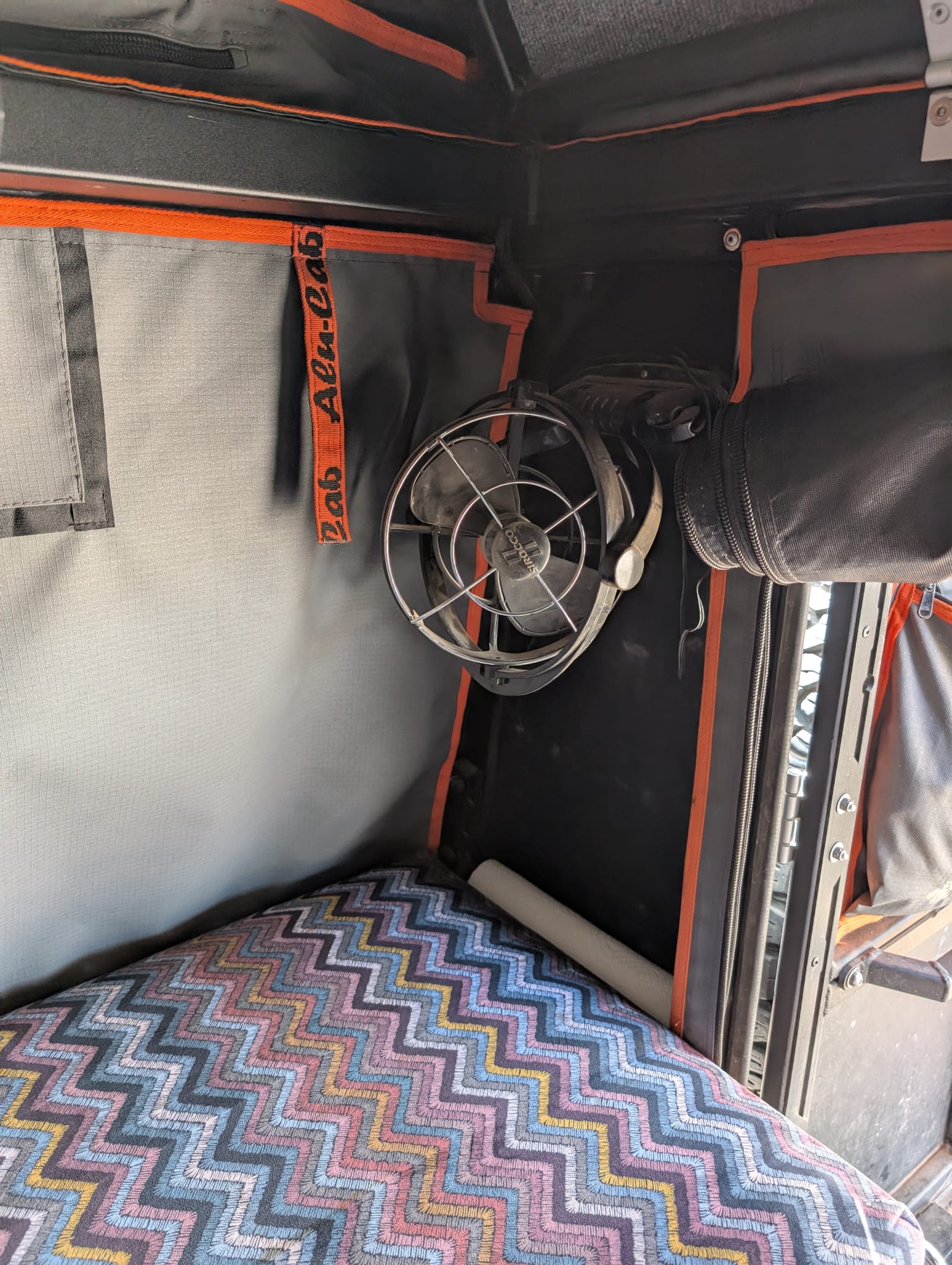 Inside a cozy RV rental: colorful zigzag bed, mounted Sirocco fan, and Alu-Cab interior features.. RAM Truck, ALucab camper 2500 2021