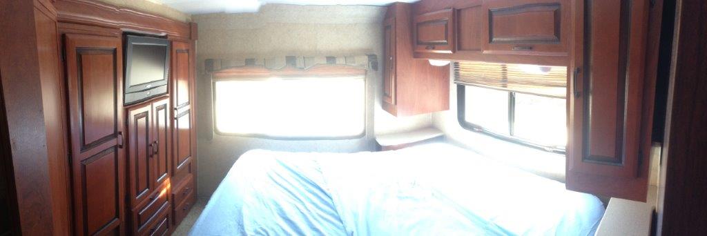 Interior of an RV rental bedroom with wooden cabinets, a TV, and bright windows over a bed.. Forest River Sunseeker 2011
