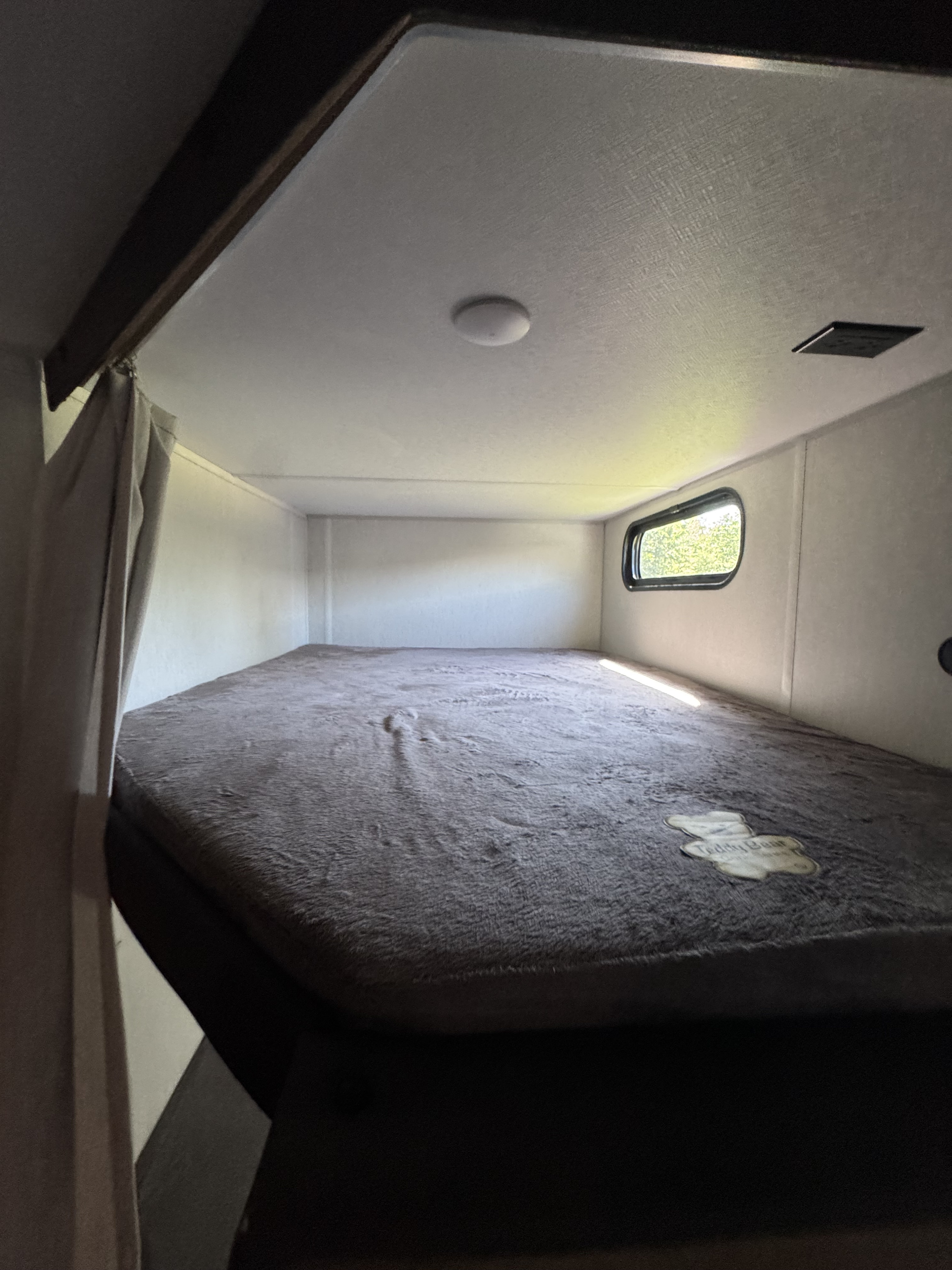 RV rental interior: A large, cozy bunk bed featuring a textured gray mattress, small window, and ceiling light.. Forest River Cherokee grey wolf black label 2024