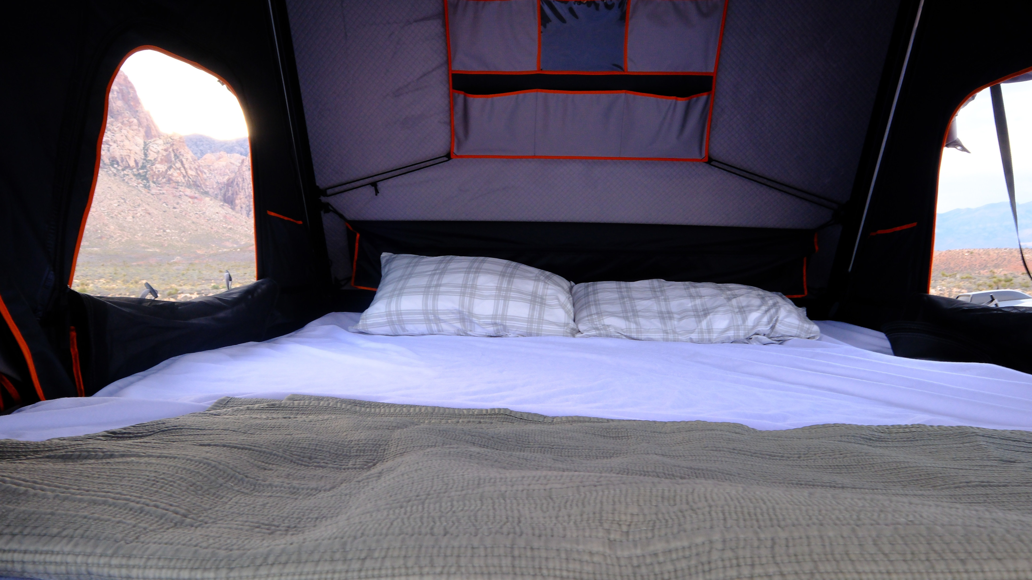 Comfortable bed inside a rooftop tent, offering stunning mountain views. Ideal for your next RV rental adventure.. Ford Van 2024