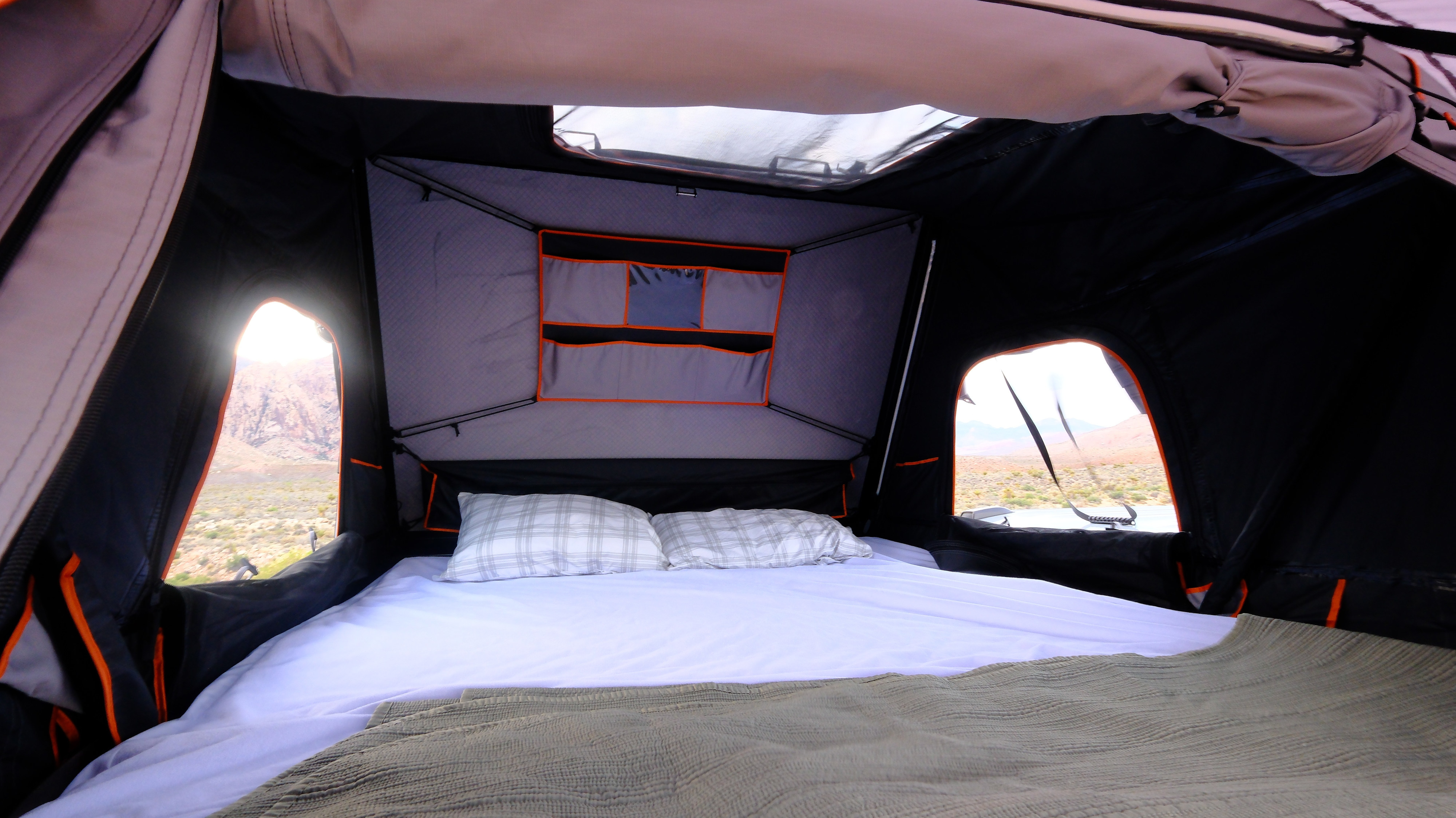 Relax in your RV rental's rooftop tent. A comfortable bed with pillows, surrounded by desert mountains for adventurous travel.. Ford Van 2024