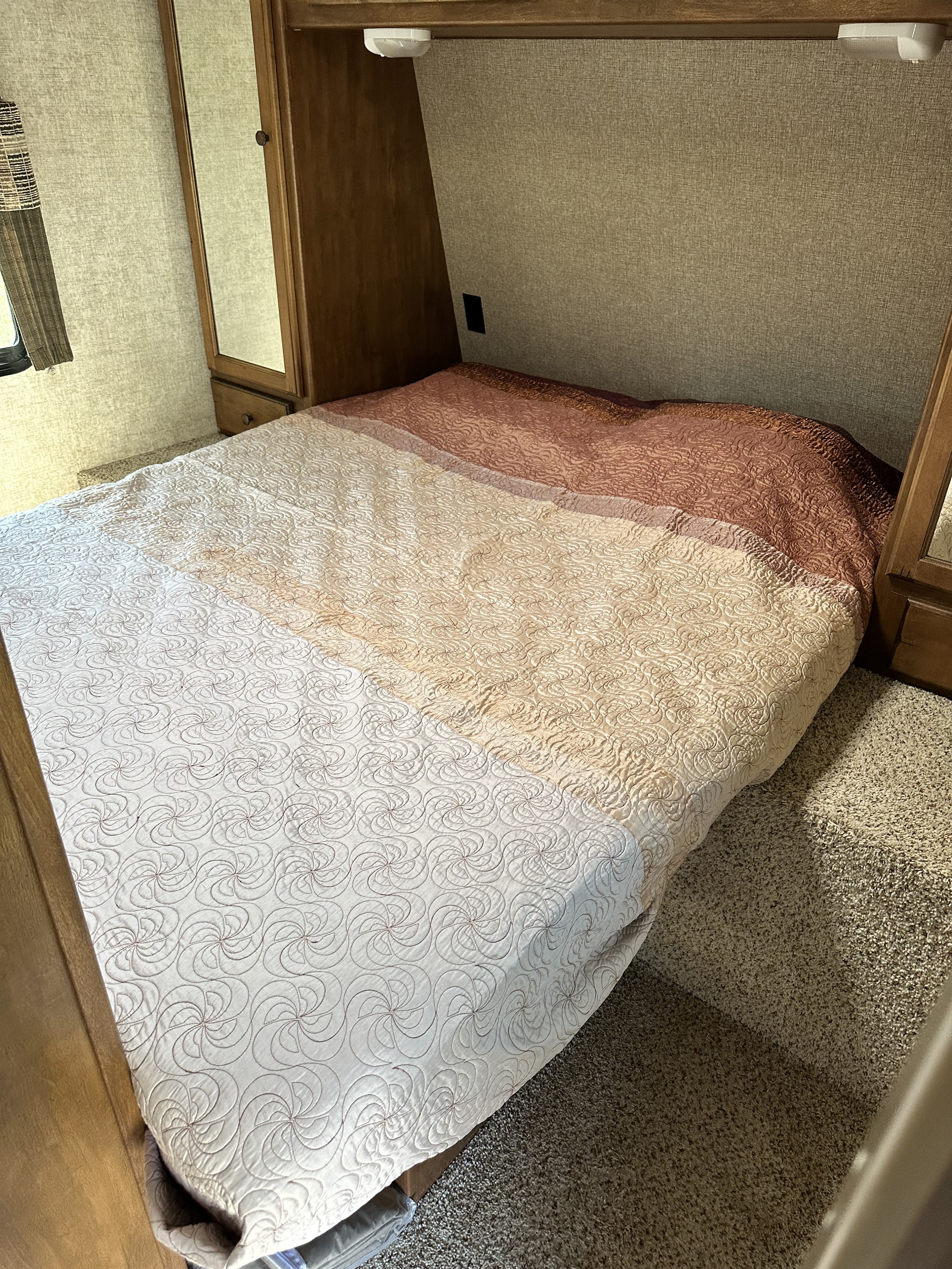 Experience comfort in this RV rental's bedroom. Features include a cozy bed with a gradient quilt, built-in storage, and carpeted floor.. Keystone RV Sprinter Campfire Edition 2015
