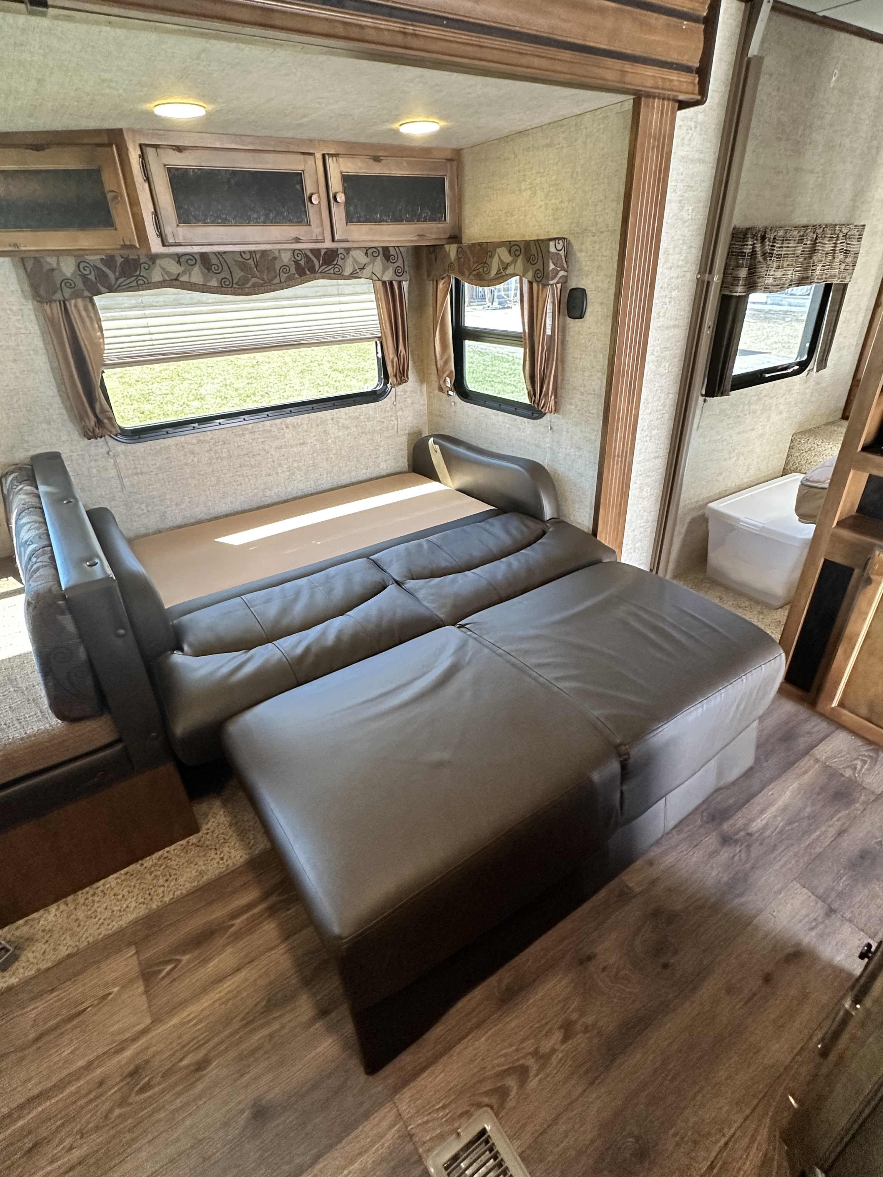 RV rental interior featuring a comfy pull-out sofa bed, overhead cabinets, and sunny windows.. Keystone RV Sprinter Campfire Edition 2015