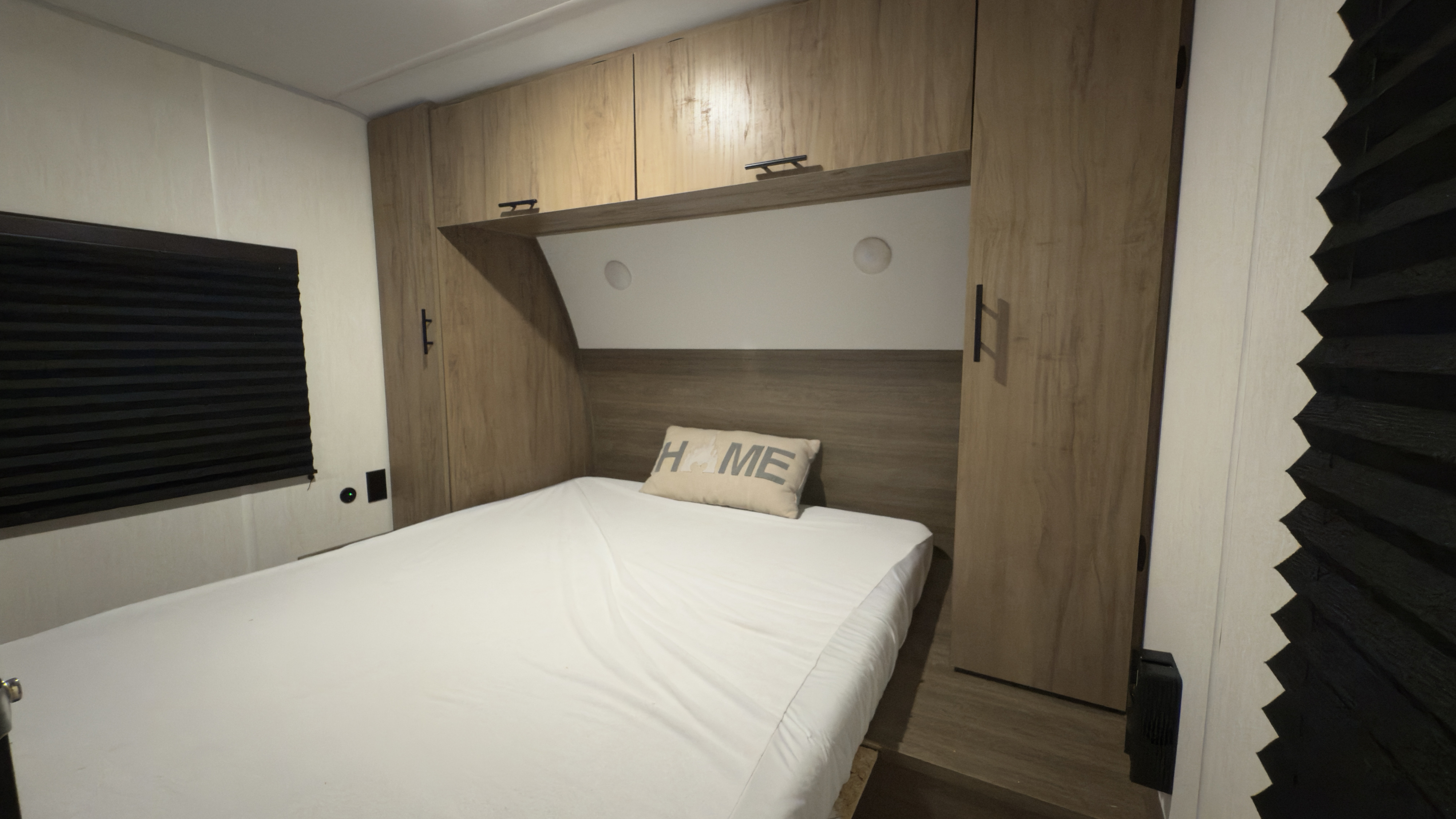 RV rental bedroom: A compact space with white bed, wood-look cabinets & black pleated blinds on the left.. Forest River Grey Wolf 23DBH 2025