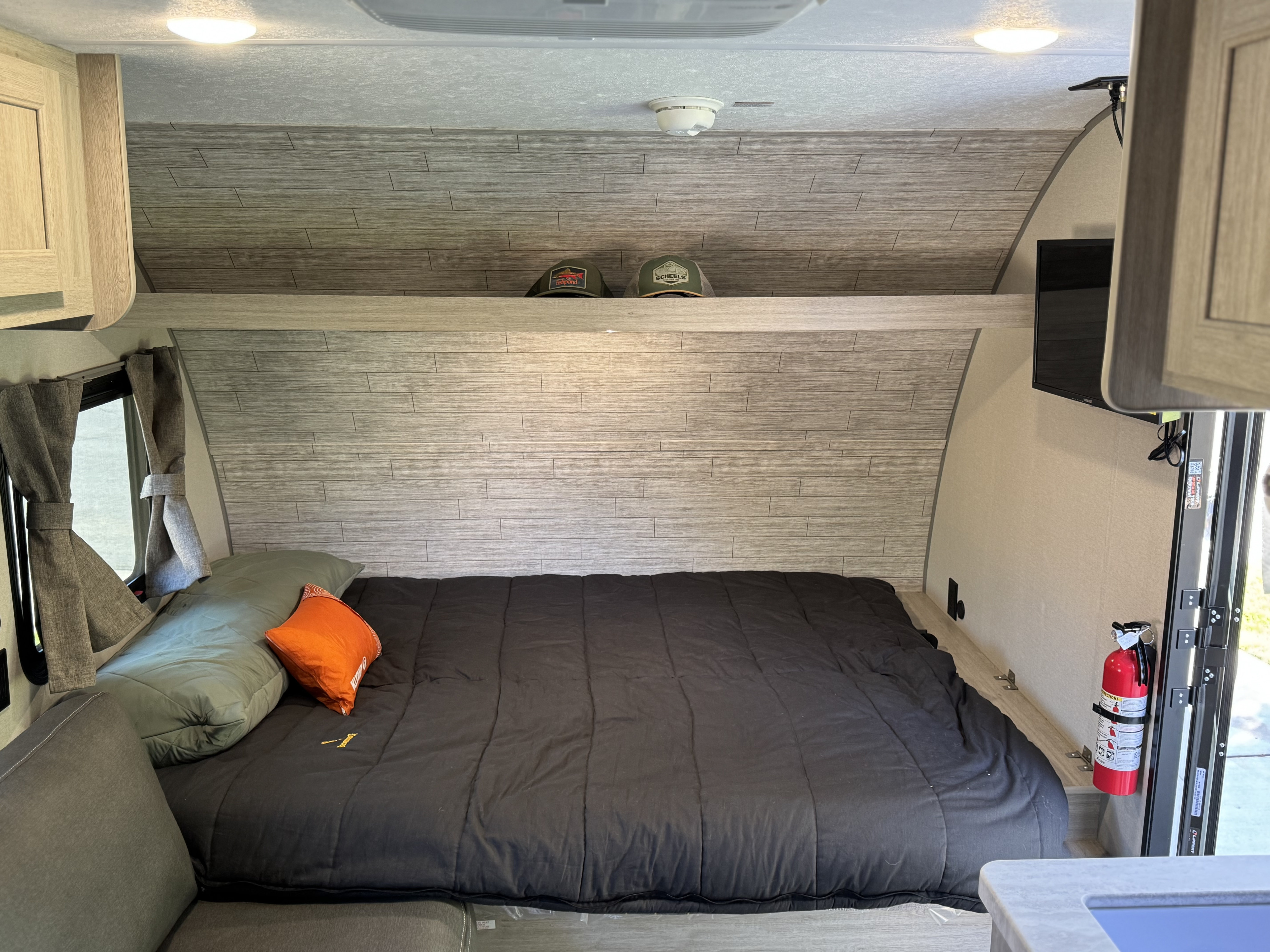 RV rental bedroom featuring a comfortable bed, light wood-look walls, overhead storage, TV, and safety gear.. Forest river Aurora light 16BHX 2025