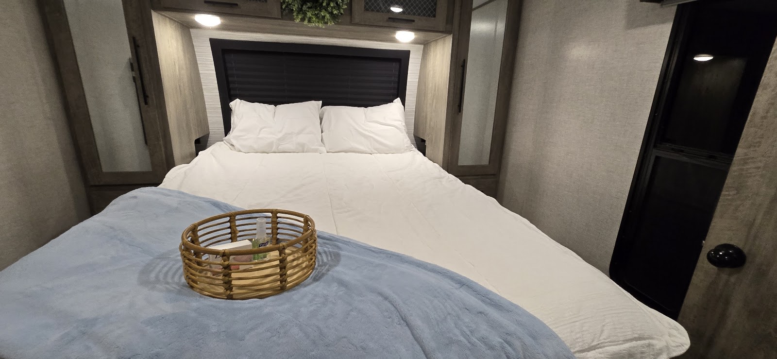 Inside an RV rental: a compact bedroom with a bed, white linens, blue blanket, and wicker basket, surrounded by built-in cabinets.. Forest River Salem Hemisphere 2021