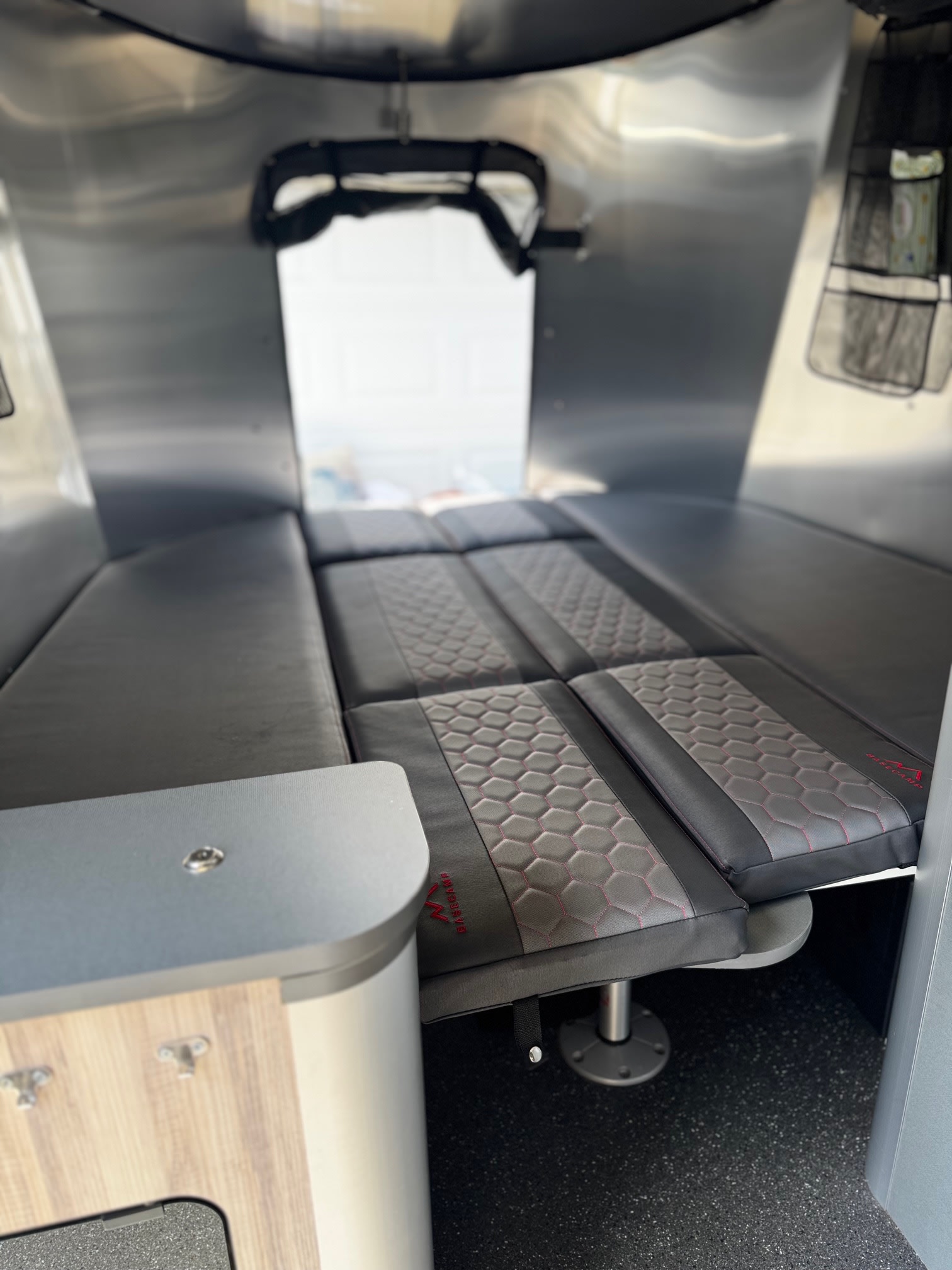 RV rental interior showing a convertible bed with gray/black hexagonal patterned cushions and sleek silver walls.. Airstream Basecamp 2021