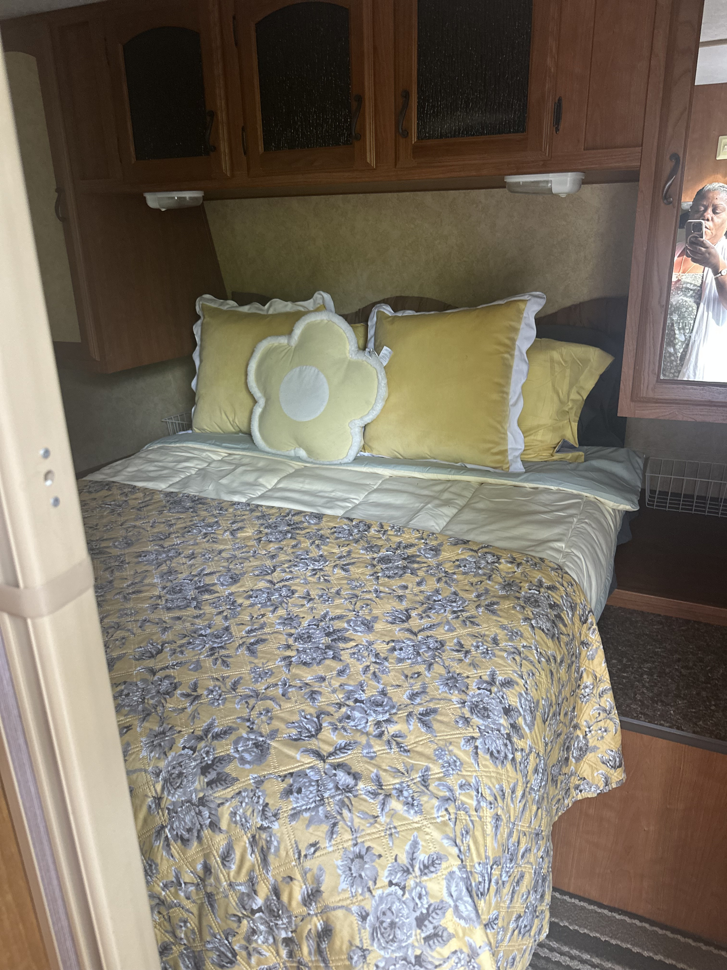 Cozy RV rental bedroom: yellow/grey floral bedding, pillows, wood cabinets, with a mirror reflection of the photographer.. Forest River Tracer Ultra Lite 2012