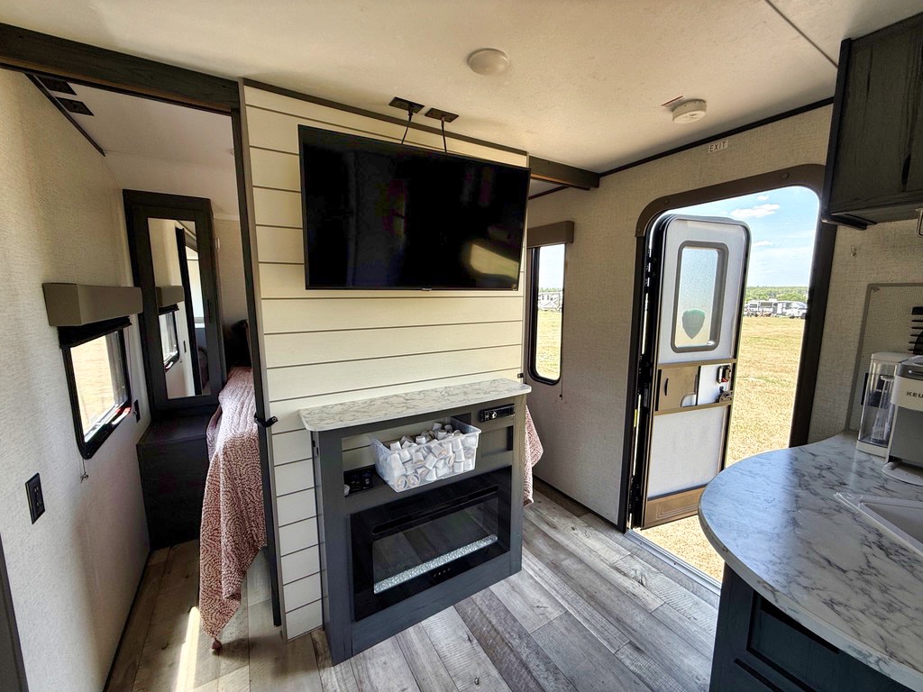 Explore this comfy RV rental interior. It features a living area with TV/fireplace, bedroom access, and an open door view.. Aspen Trail LE 2021